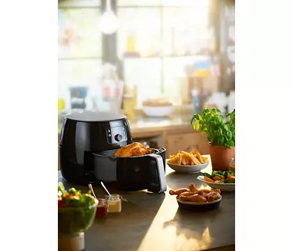 An air fryer with chicken and sides on a countertop, with a bright background.