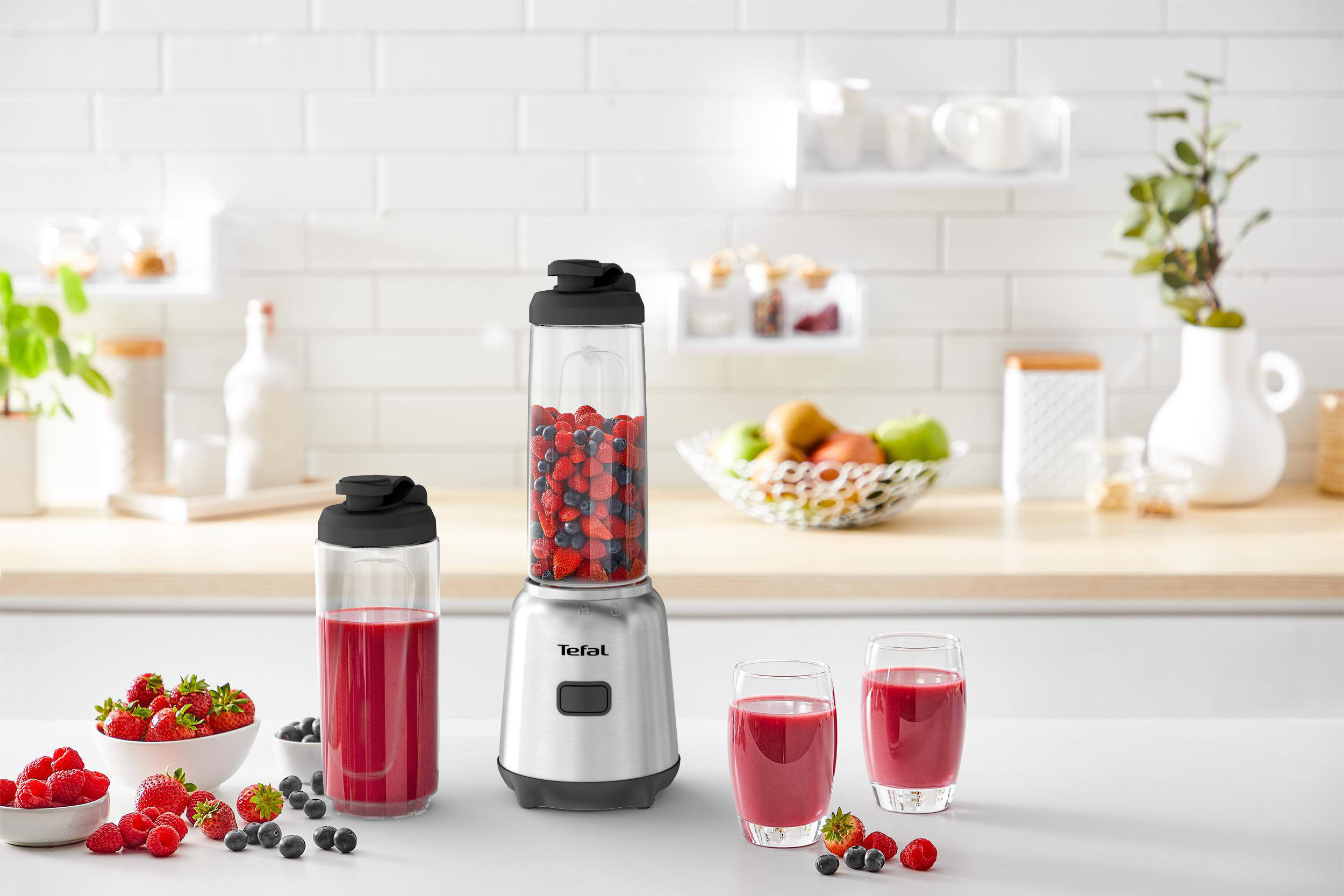 Mixer mit Früchten und zwei Smoothie-Gläsern, auf weißer Küchentheke.