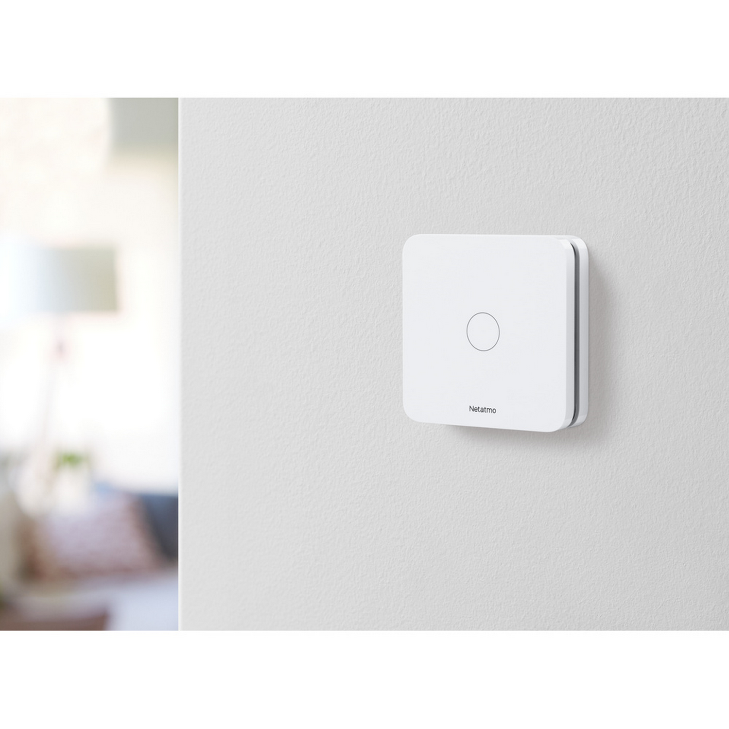 Un dispositivo Netatmo blanco en una pared blanca con un pequeño círculo. Fondo borroso.