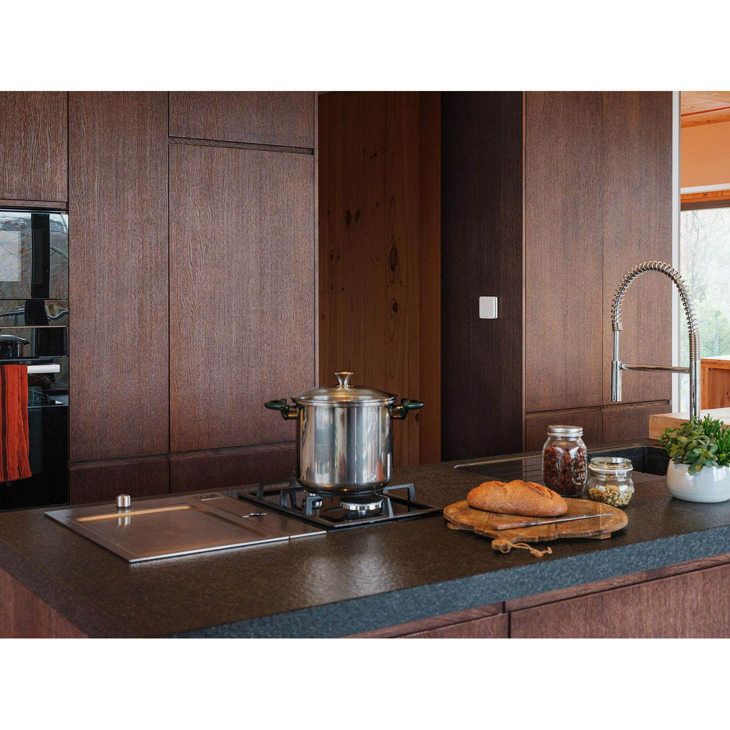 Una escena de cocina con una placa de cocina, una olla y una tabla de pan en una encimera con gabinetes de madera.