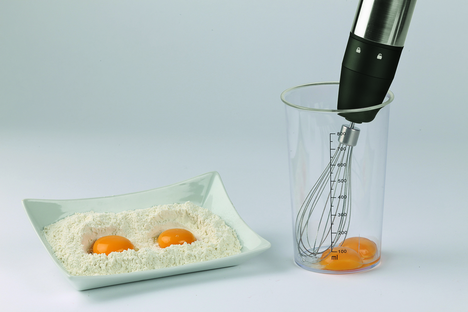 Deux jaunes d'œufs dans la farine et un mixeur dans une tasse à mesurer.
