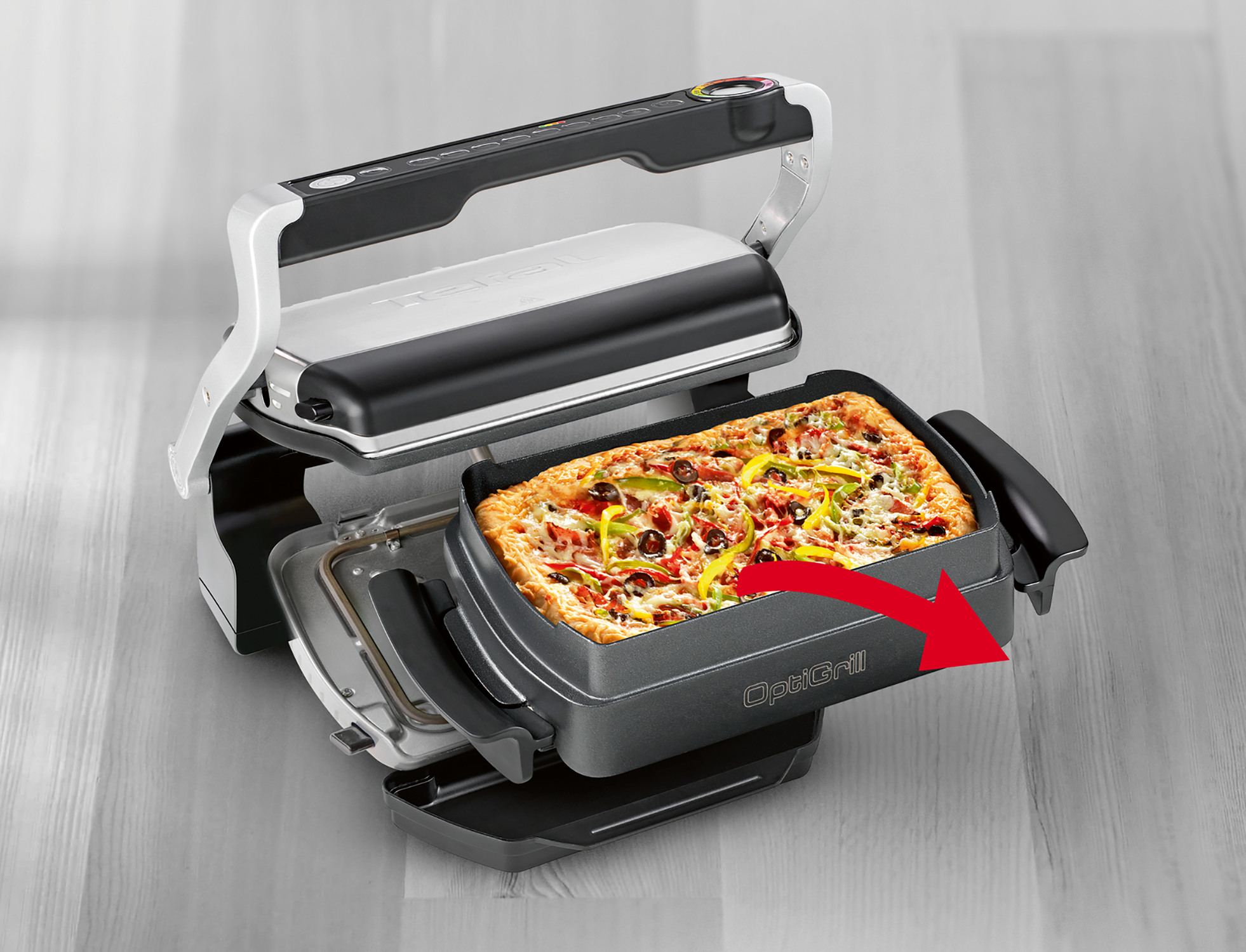 An open grill with a pizza inside. A red arrow points towards the removable tray.