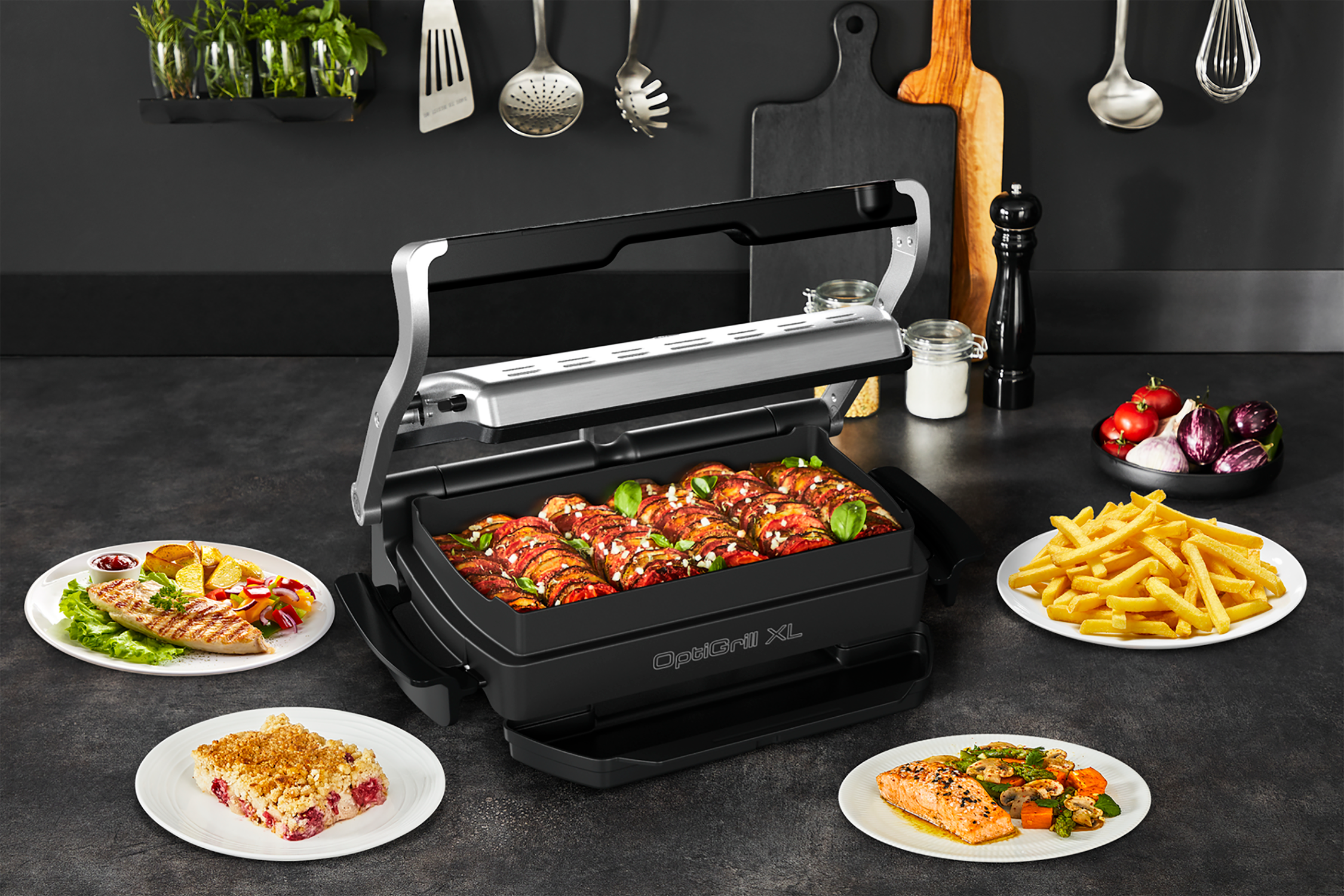 Open grill with various cooked foods on plates, on a black kitchen counter.
