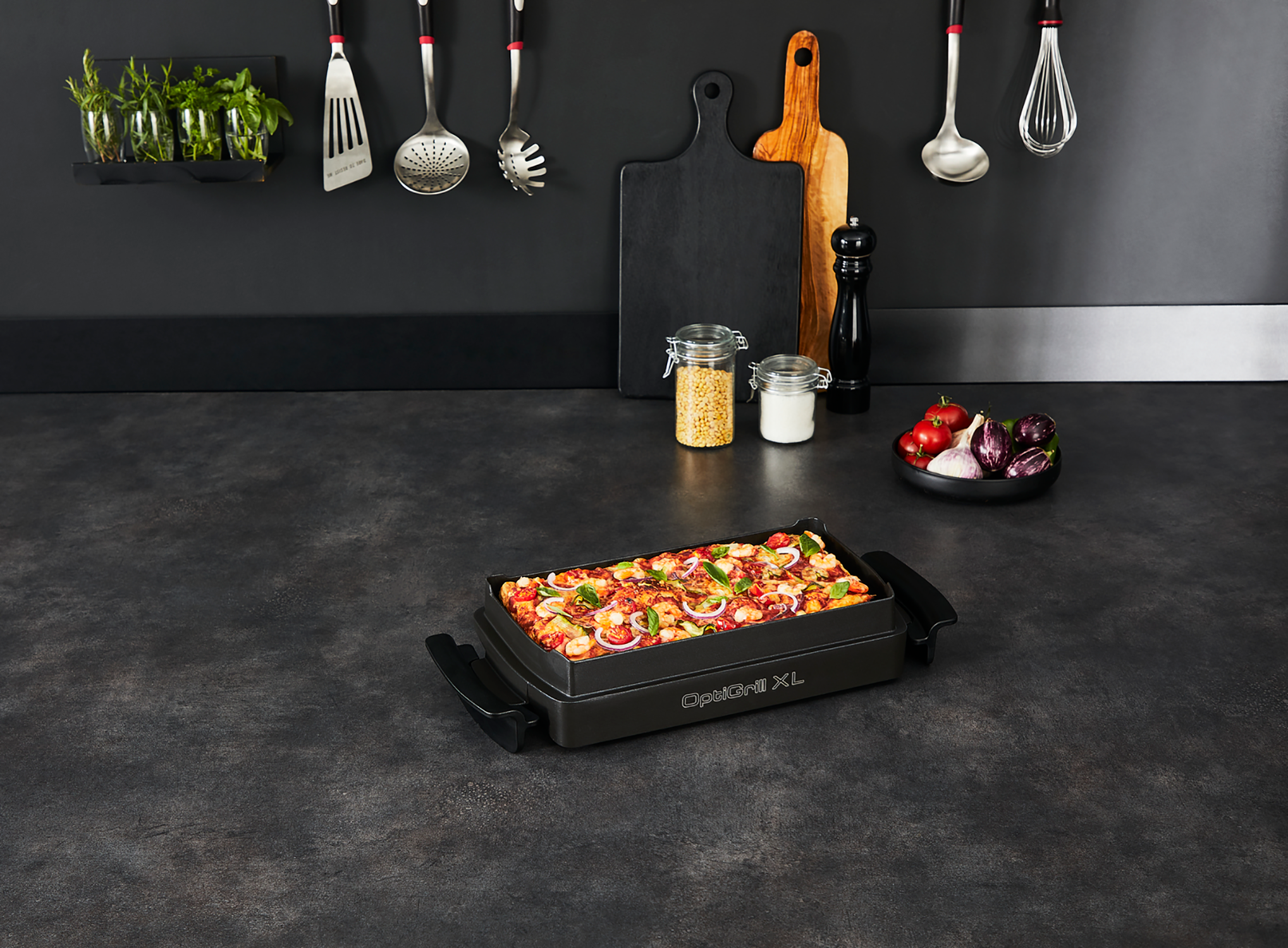 A kitchen countertop with a black OptiGrill XL grill. Kitchen utensils and food items are visible.