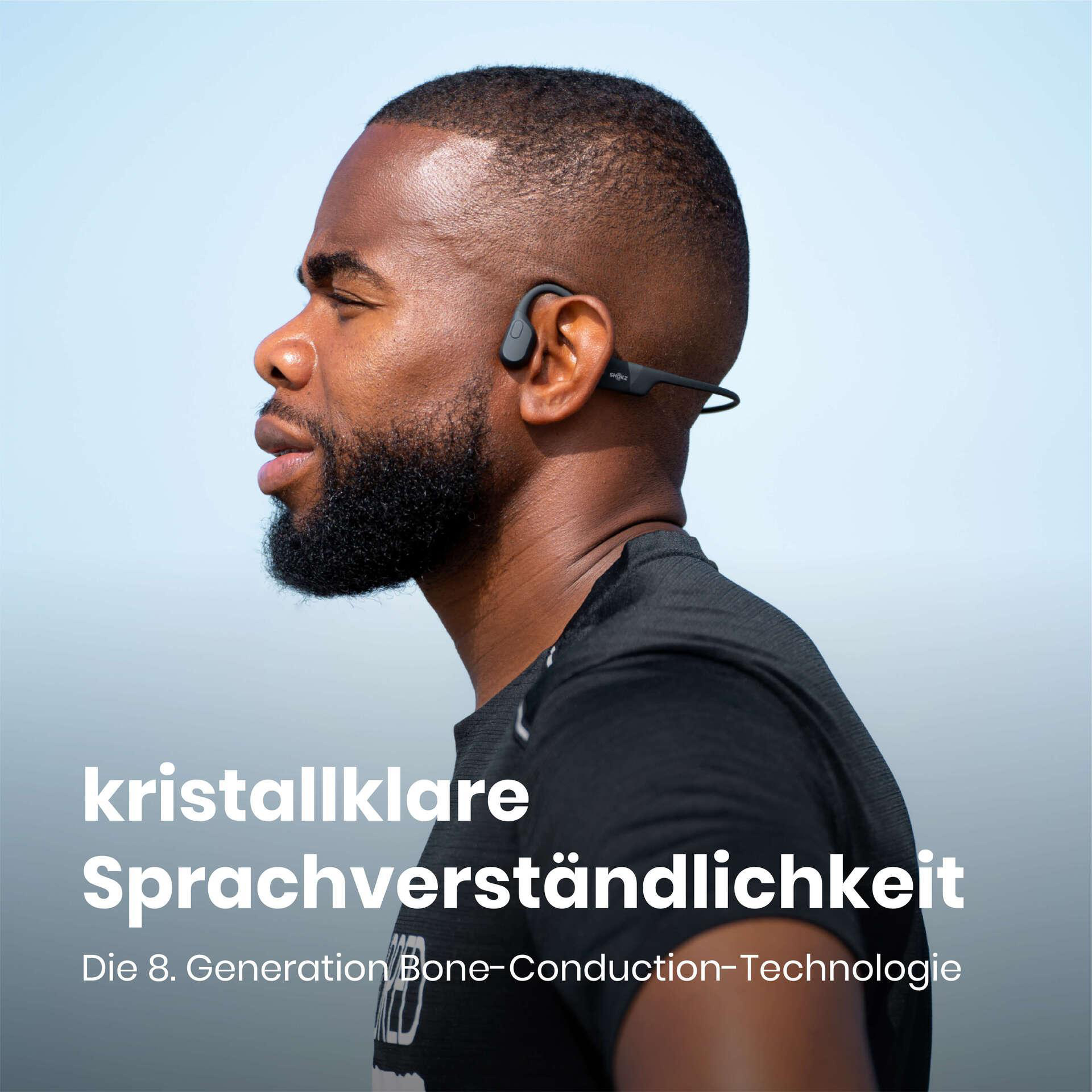 Ein schwarzer Mann mit schwarzen Knochenschallkopfhörern, der nach links schaut. Der Hintergrund ist hellblau.