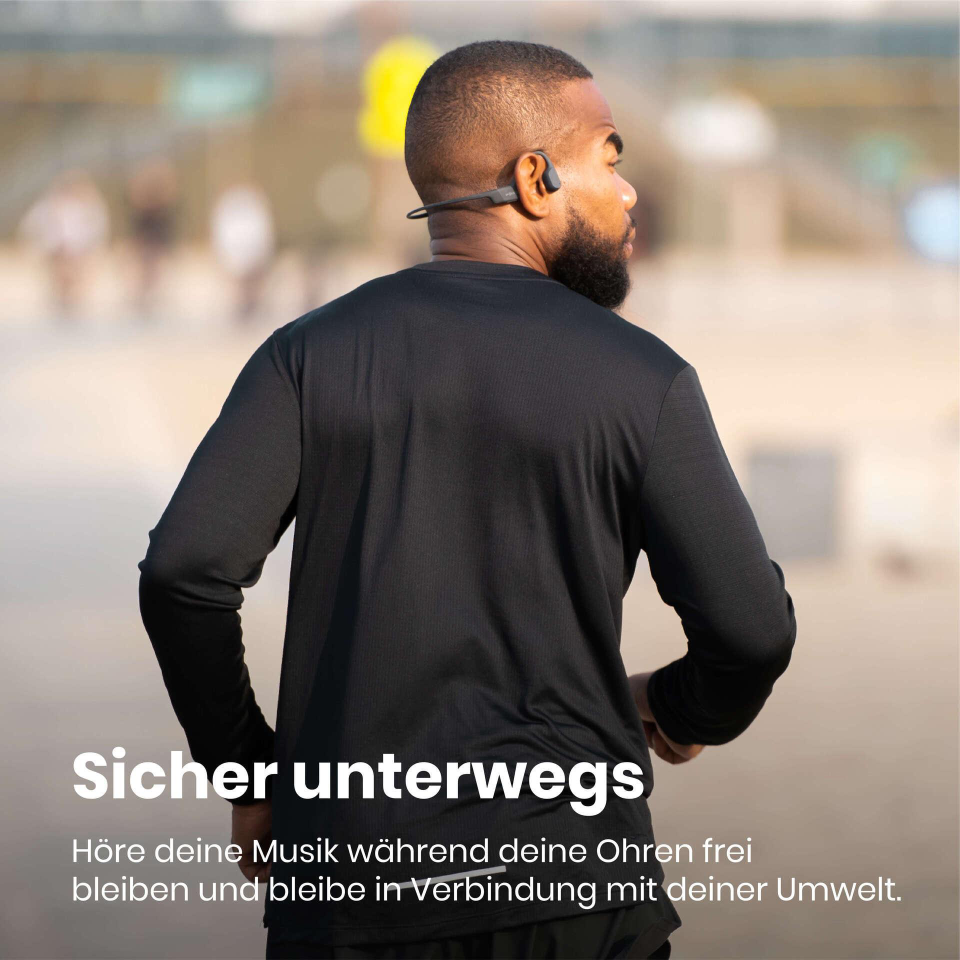Mann in schwarzem Hemd mit Knochenschallkopfhörern, der im Freien läuft. Der Hintergrund ist unscharf.