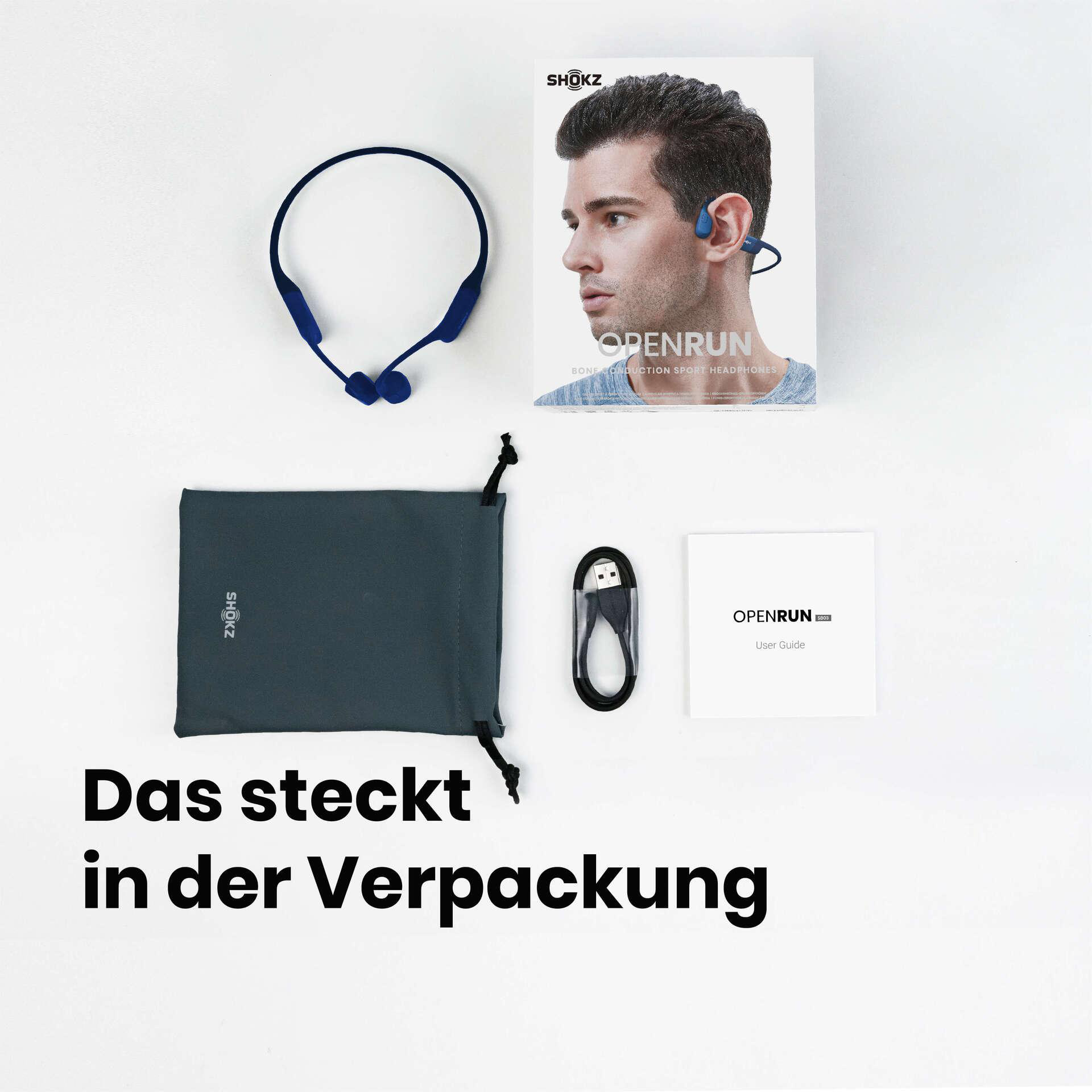 Das Bild zeigt Shokz OpenRun-Kopfhörer und Zubehör: Hülle, Kabel und Benutzerhandbuch, angeordnet auf weißer Oberfläche.