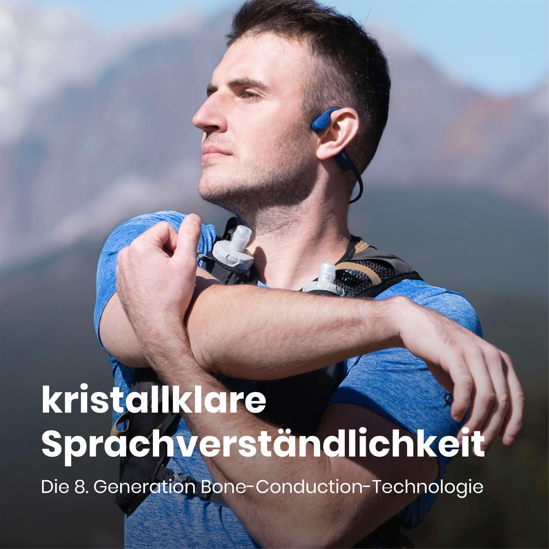 Ein Mann trägt blaue Kopfhörer. Er ist draußen mit Bergen im Hintergrund. Text: kristallklare Sprachverständlichkeit.