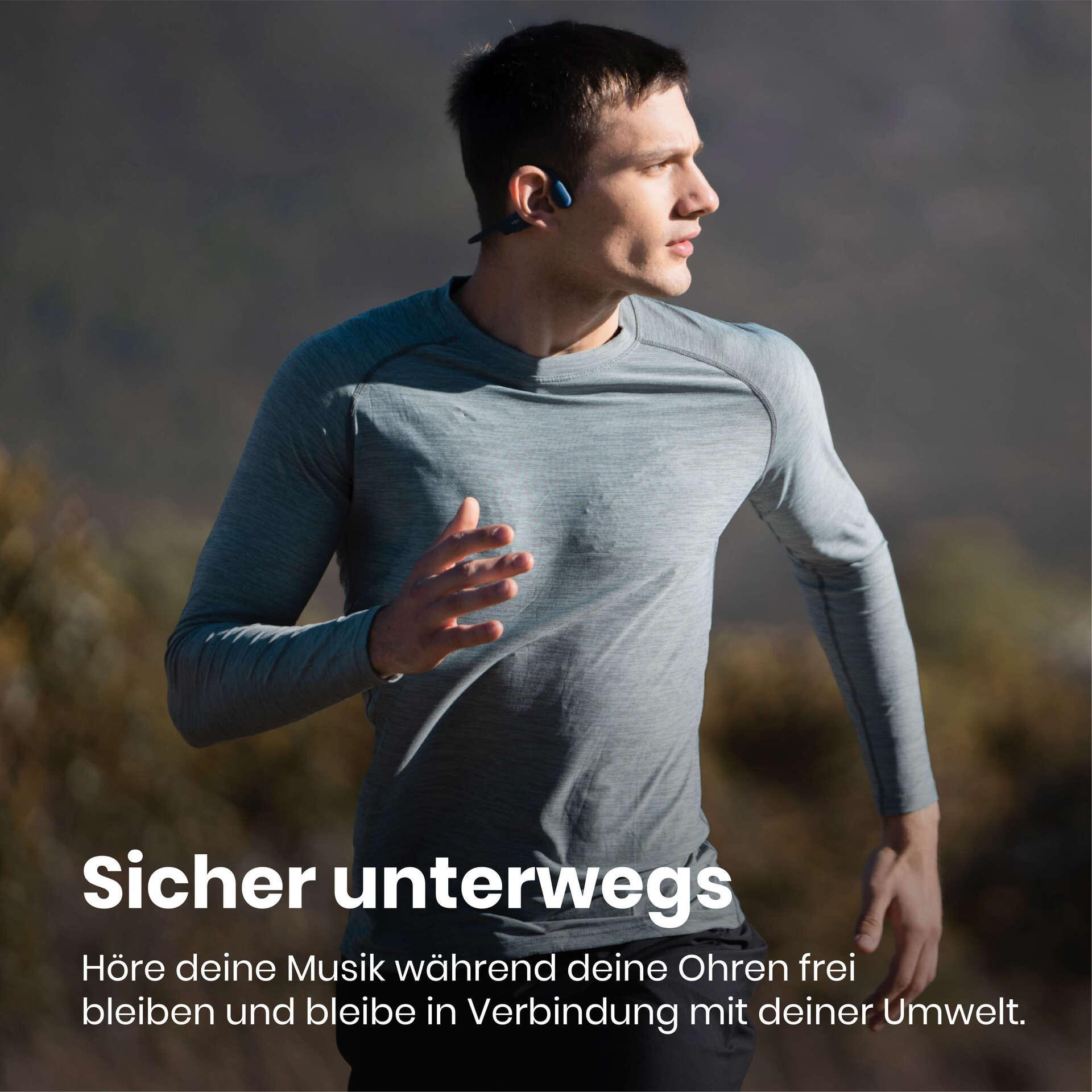 Mann läuft mit Kopfhörern, trägt graues Hemd. Hintergrund: verschwommene Bäume. Text: Sicher unterwegs.