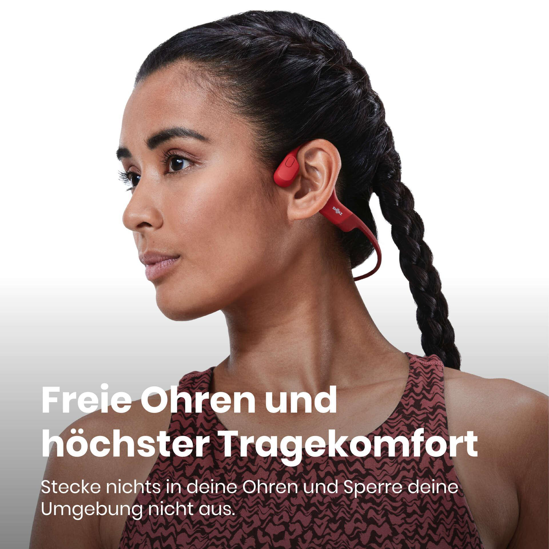 Eine Frau mit roten Kopfhörern und dunklem Zopf. Der Text lautet 'Freie Ohren und höchster Tragekomfort'.