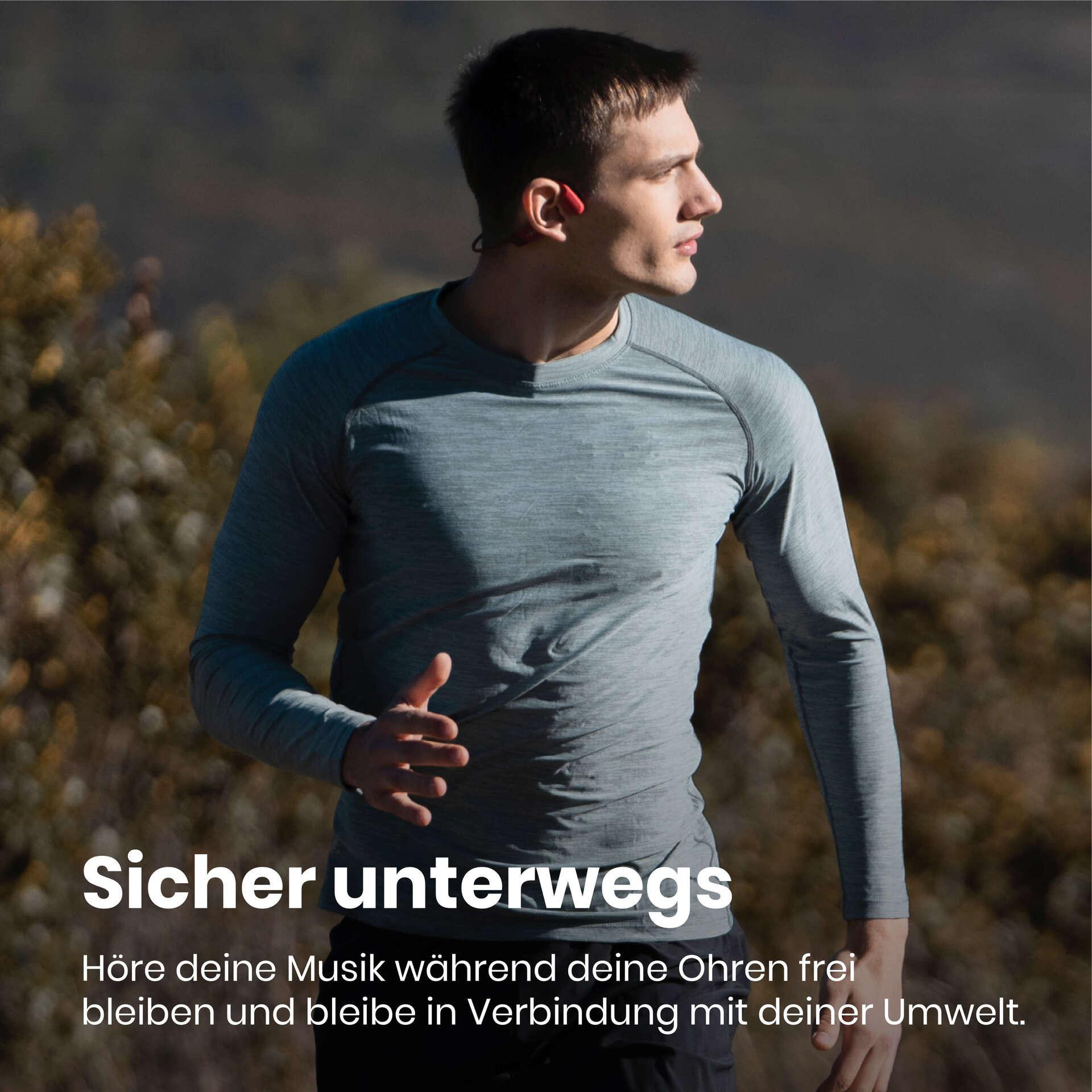 Mann läuft draußen, trägt graues Hemd, rote Ohrhörer. Text 'Sicher unterwegs' in Weiß. Verschwommener Hintergrund mit grünem Laub.