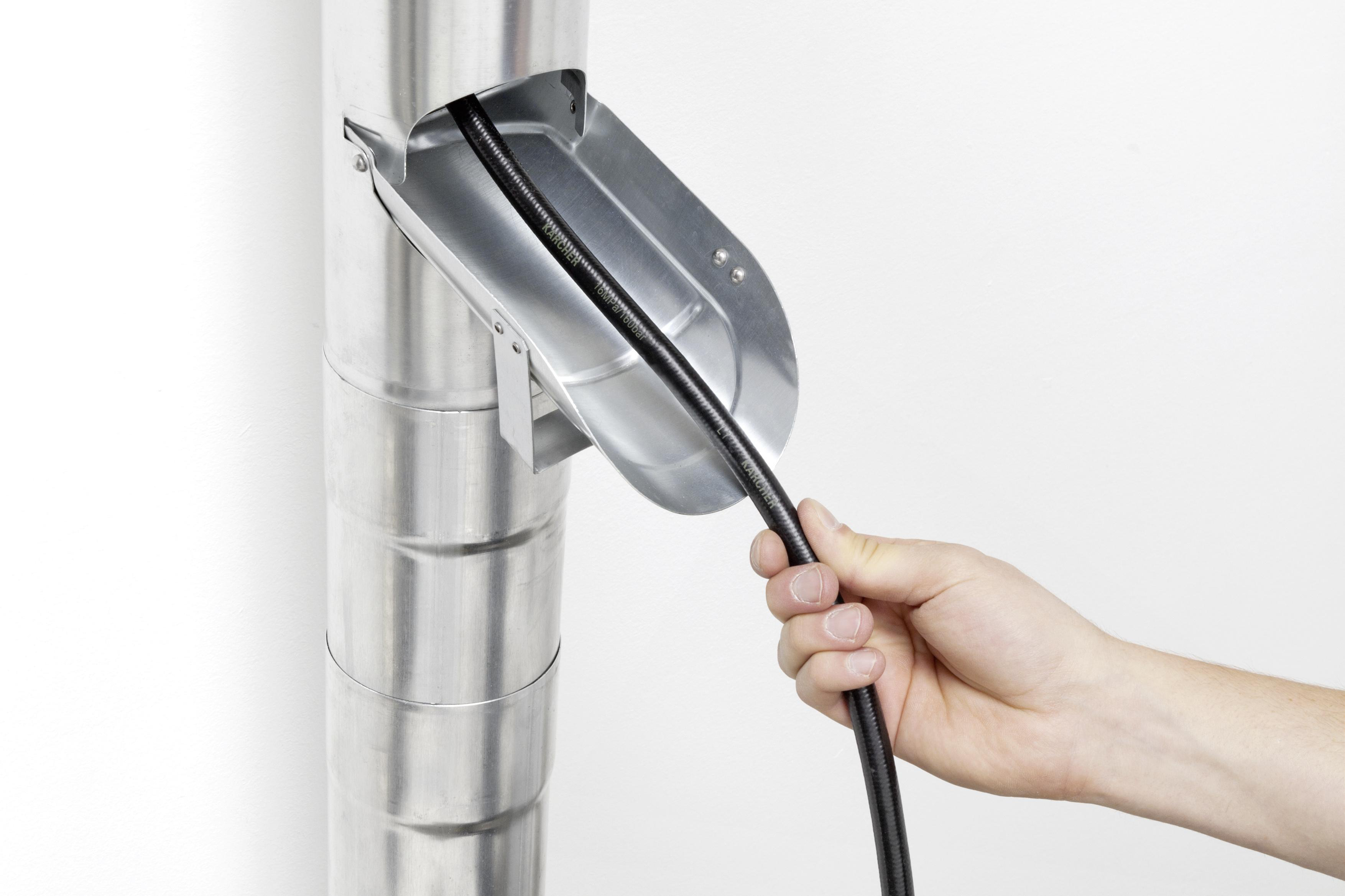 Hand, die ein schwarzes Kabel hält und es in ein metallisches Fallrohr einführt.