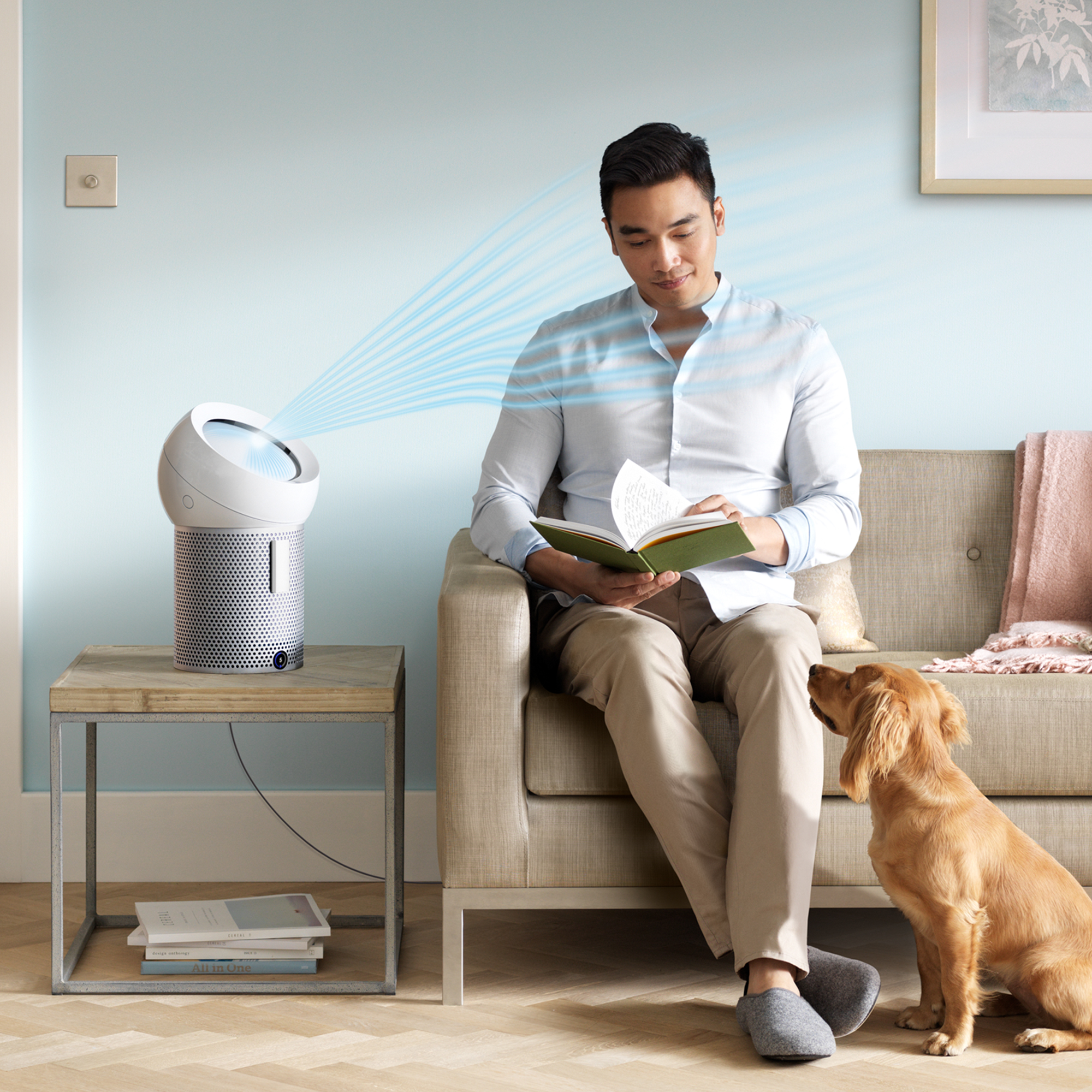 Hombre sentado con libro, purificador de aire y perro.