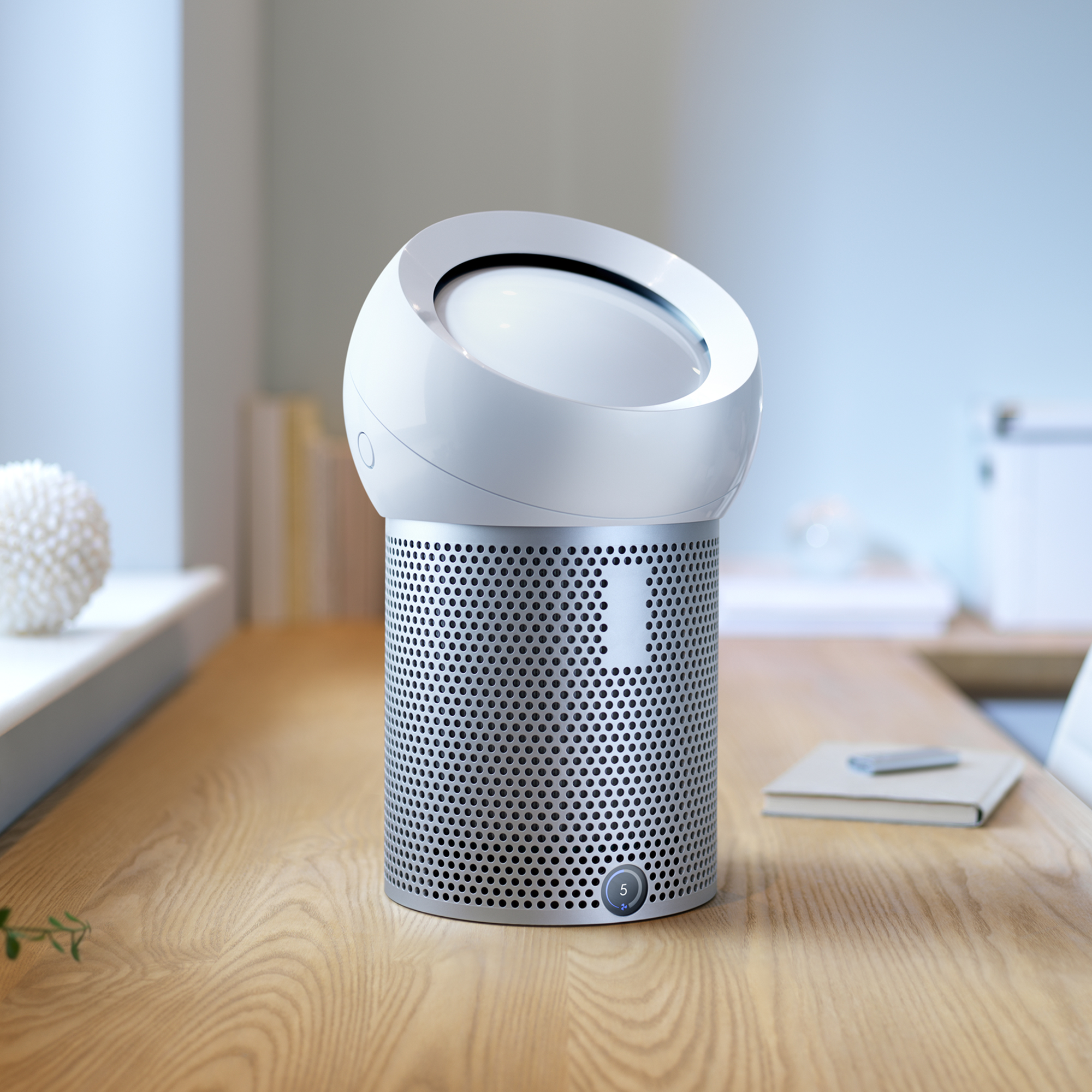 Un purificador de aire Dyson blanco sobre una mesa de madera. Tiene un diseño único con parte superior circular.