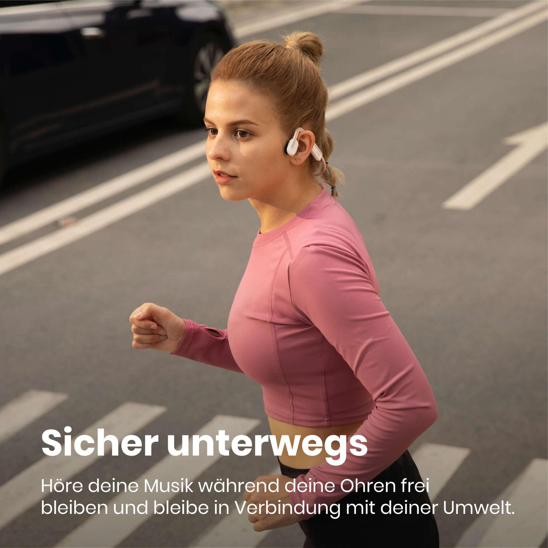 Frau joggt auf einer Straße, trägt Open-Ear-Kopfhörer. Text: Sicher unterwegs.