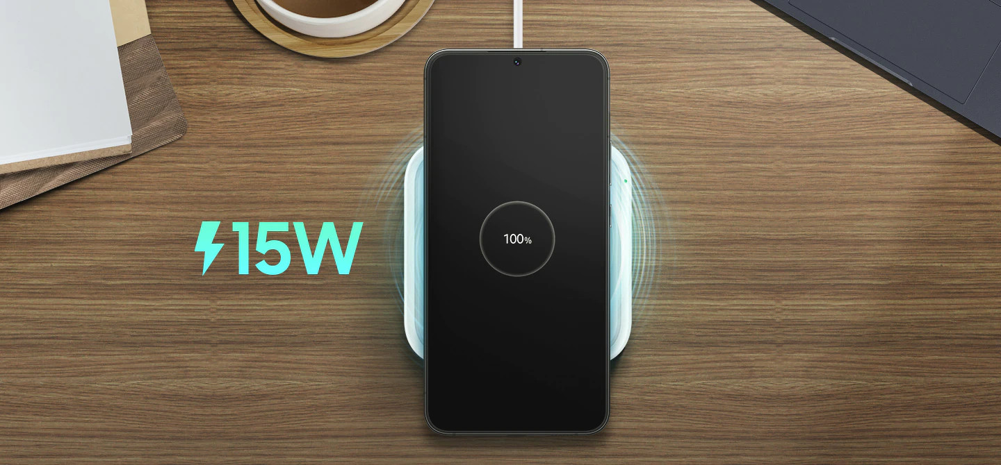 A black phone charging on a white wireless charger. Text says "15W" and "100%".