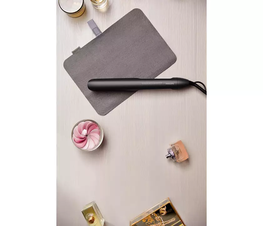 Hair straightener and accessories on a table. Includes a grey pad, perfume, and other items.