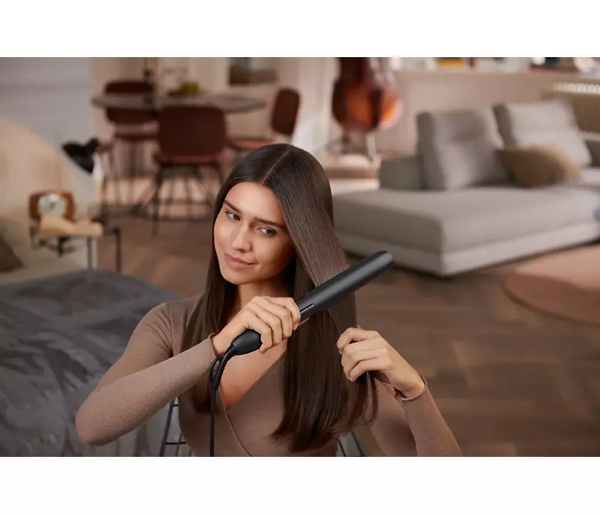 Woman using a black hair straightener, with straight hair.