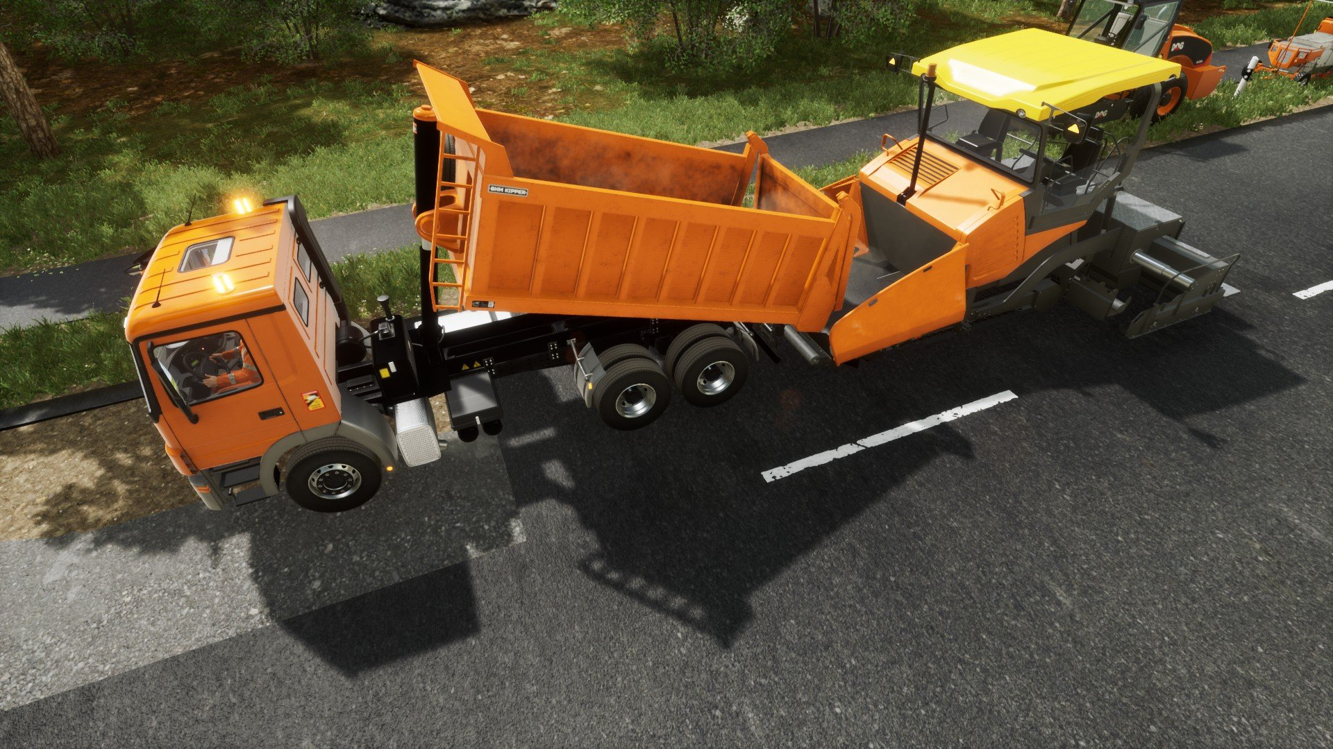 Camion arancione e finitrice che lavorano su una strada. Il camion ha un contenitore e la finitrice è gialla.
