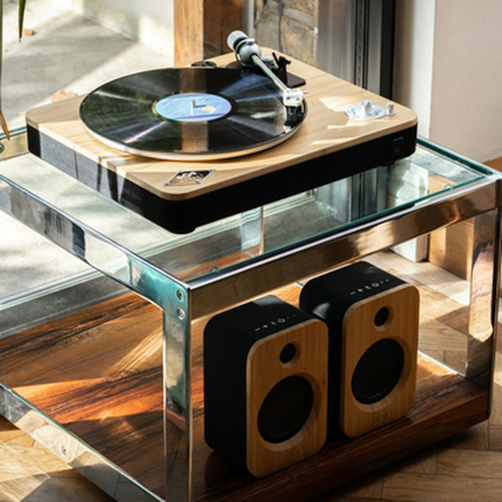 Een platenspeler met een plaat en twee luidsprekers op een glazen en metalen tafel.