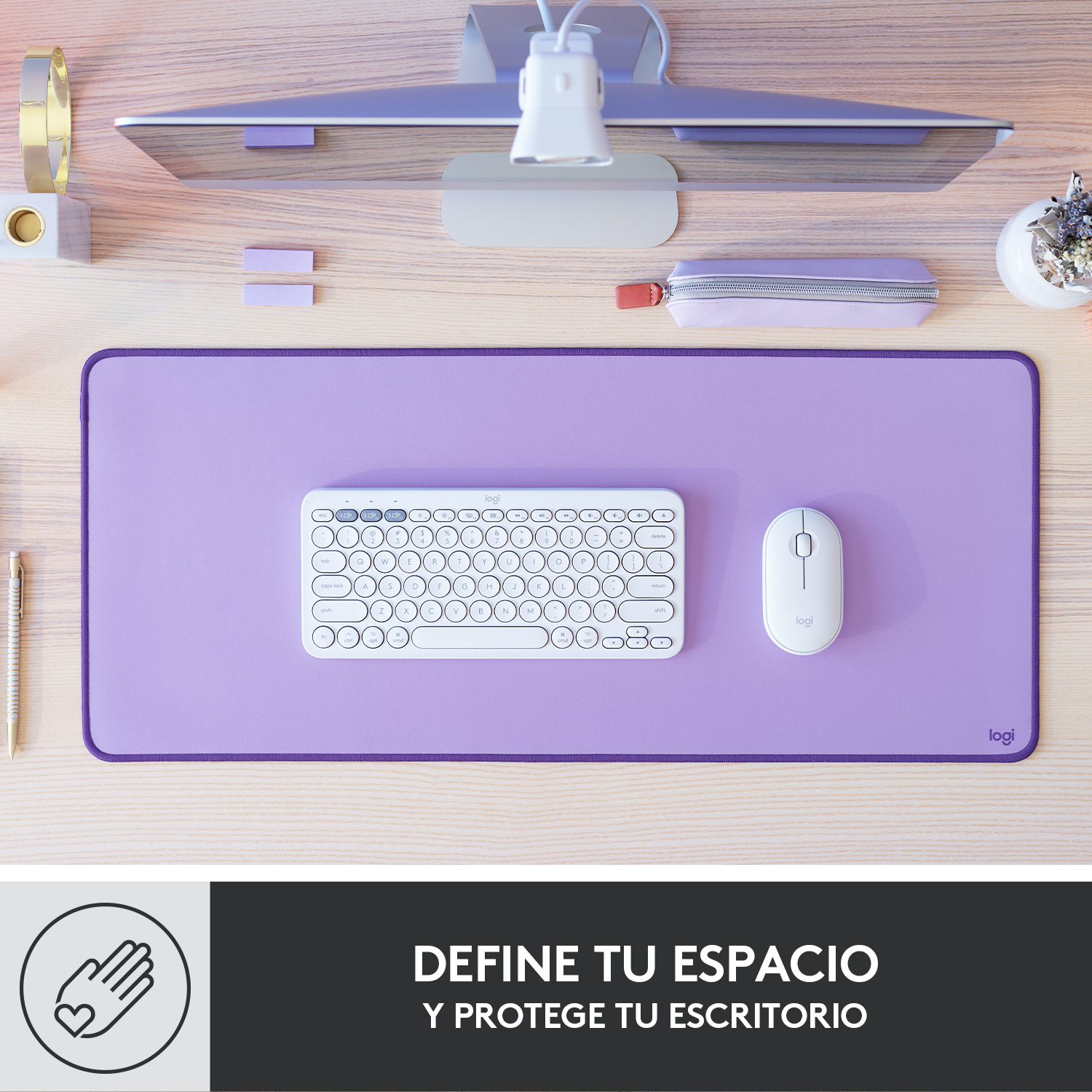 Una configuración de escritorio con un mousepad, teclado y mouse morados. Un monitor, accesorios de escritorio y texto en la parte inferior.