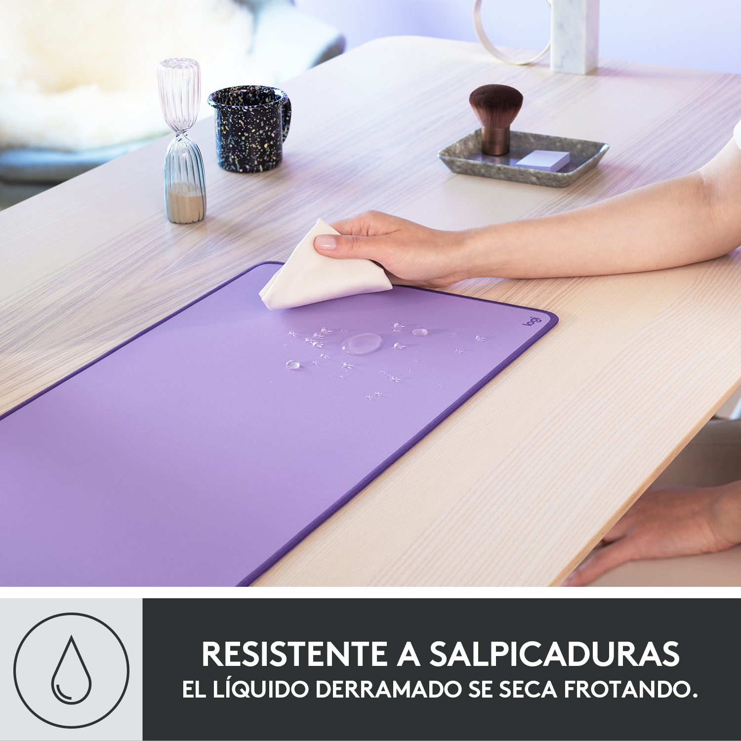 Una mano limpiando un líquido derramado en una alfombrilla de escritorio morada.