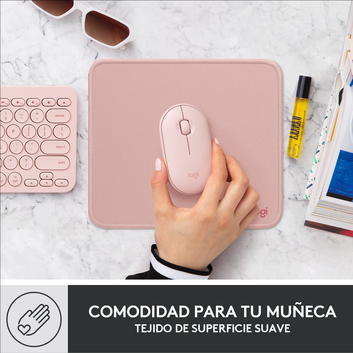 La mano de una persona sosteniendo un ratón inalámbrico rosa sobre una alfombrilla rosa.
