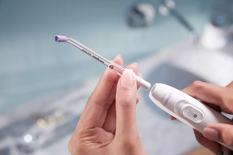 A person's hands assembling a white Philips Sonicare water flosser.