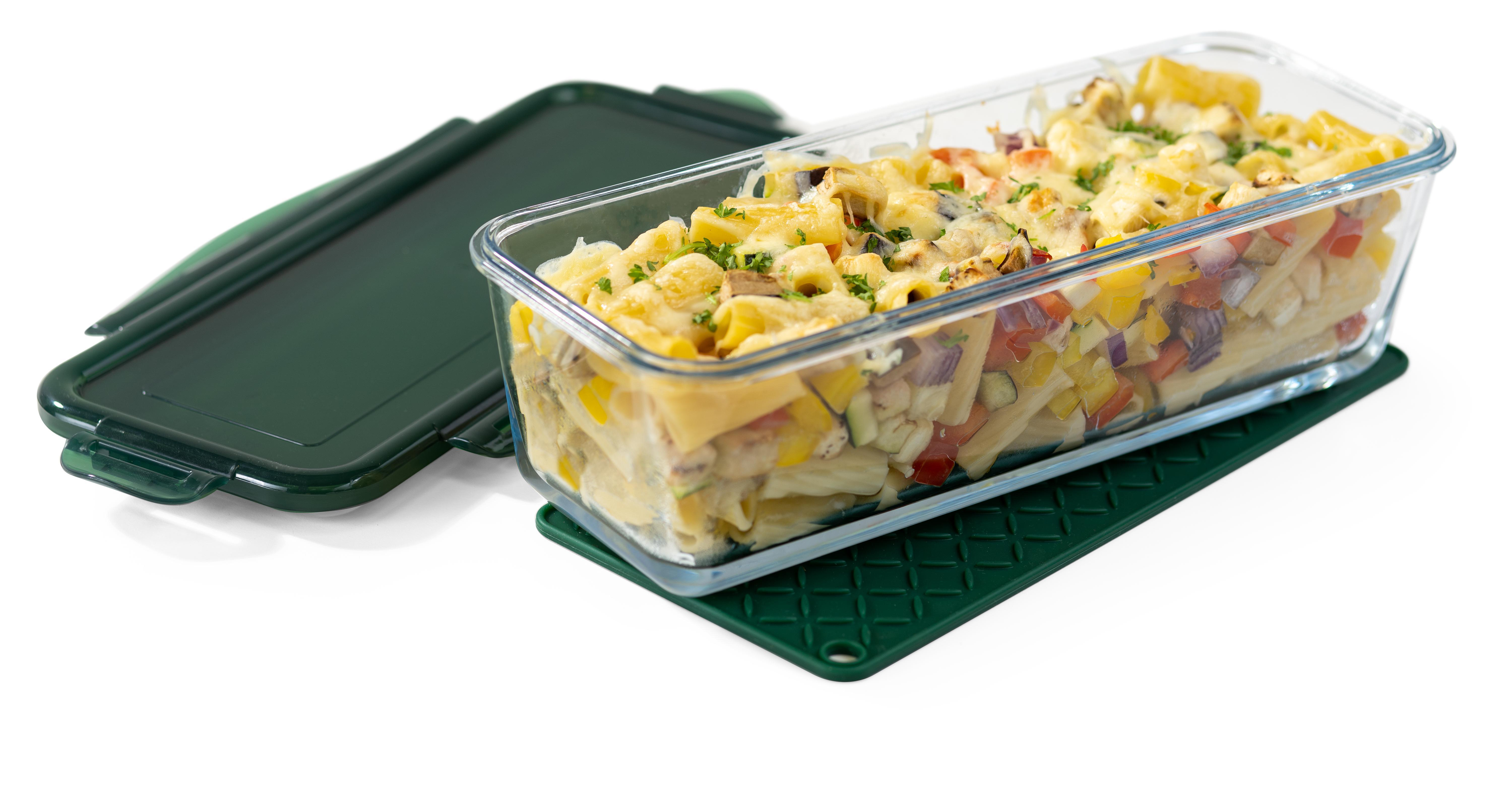 Glasbehälter mit gebackener Pasta, grünem Deckel und grüner Matte auf weißer Oberfläche. Deckel leicht geöffnet.