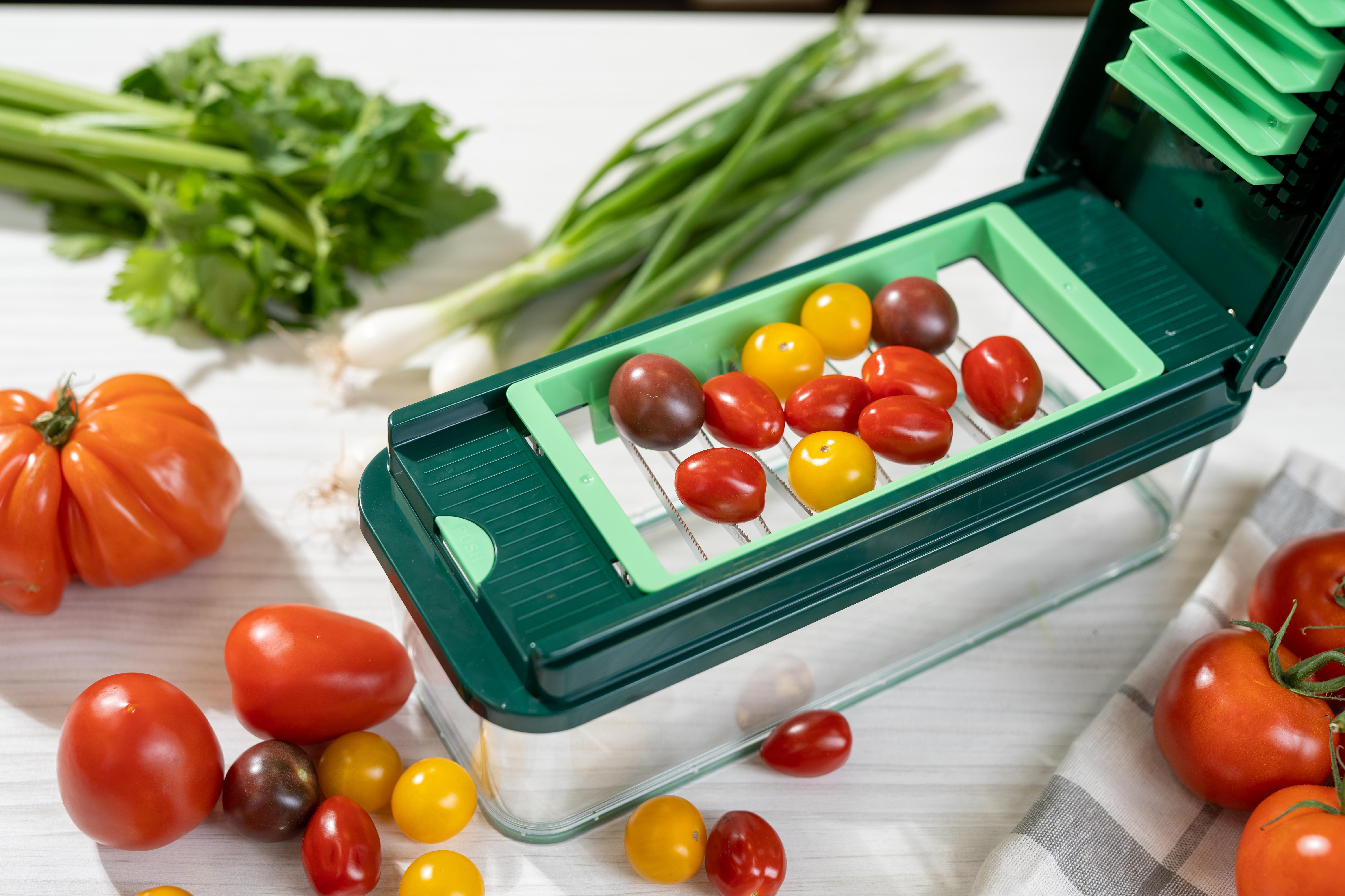 Ein grüner Zerkleinerer mit Tomaten und Frühlingszwiebeln. Auch Tomaten und Sellerie auf weißer Oberfläche.