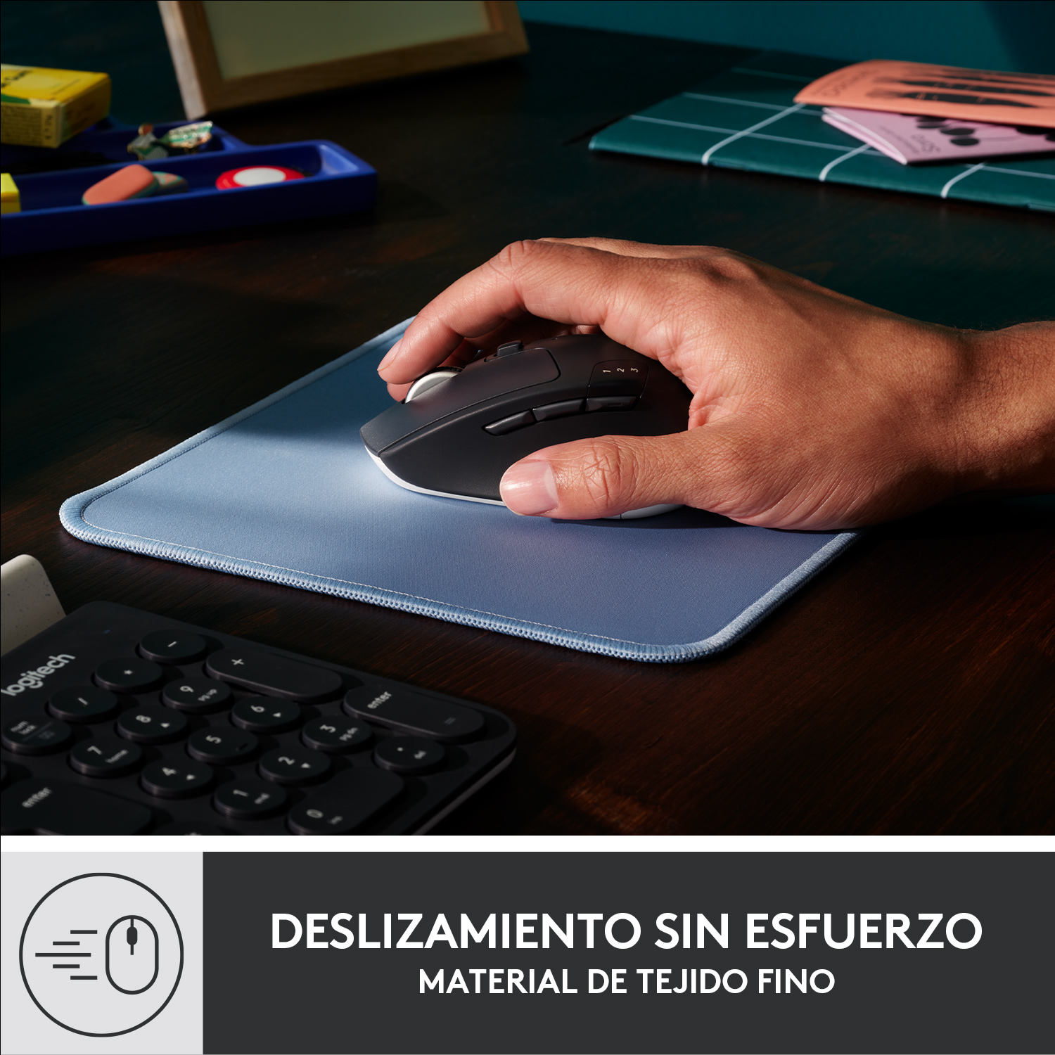 Mano usando un ratón de ordenador sobre una alfombrilla azul. Teclado en el fondo.