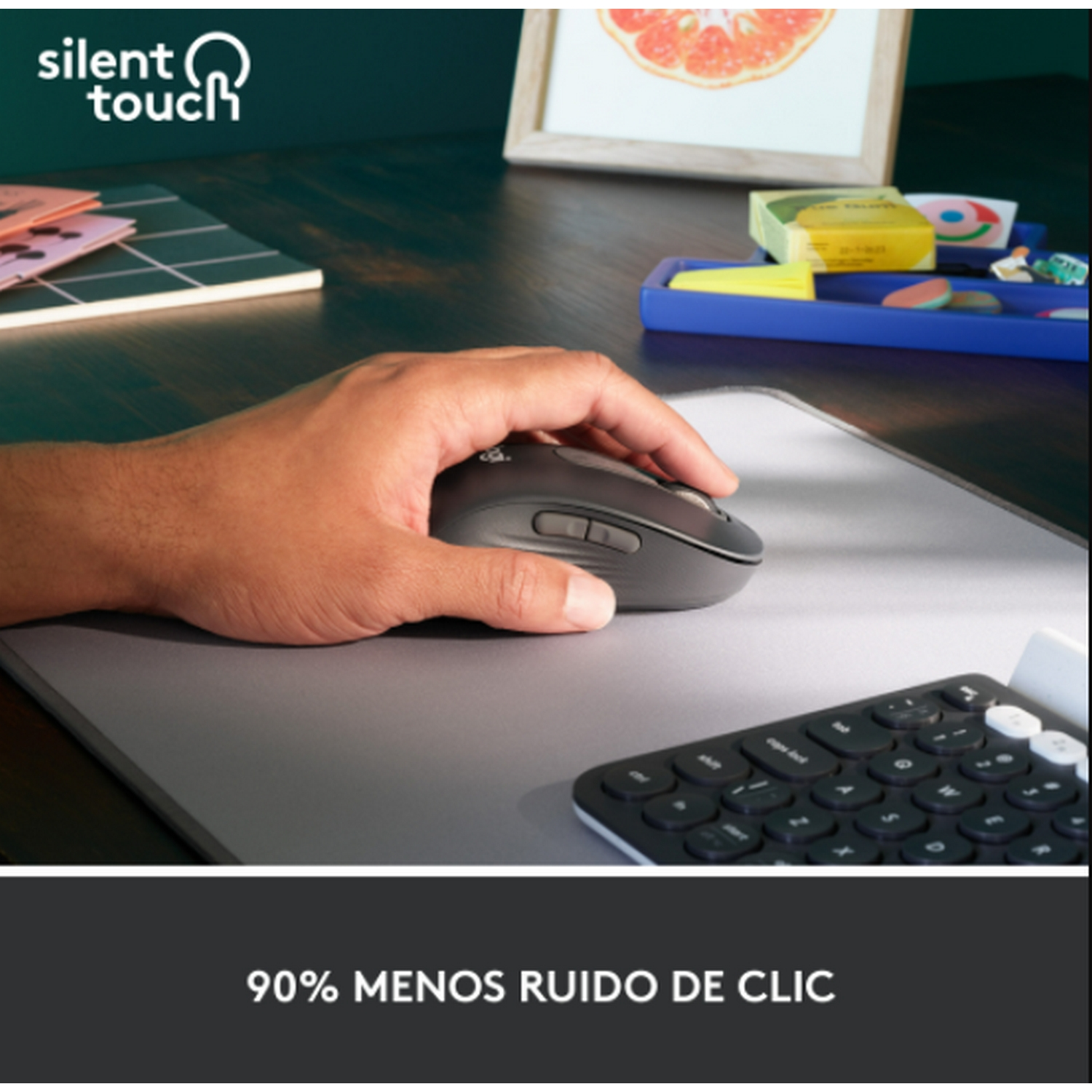 Mano usando un ratón gris oscuro sobre una alfombrilla gris con teclado atrás.