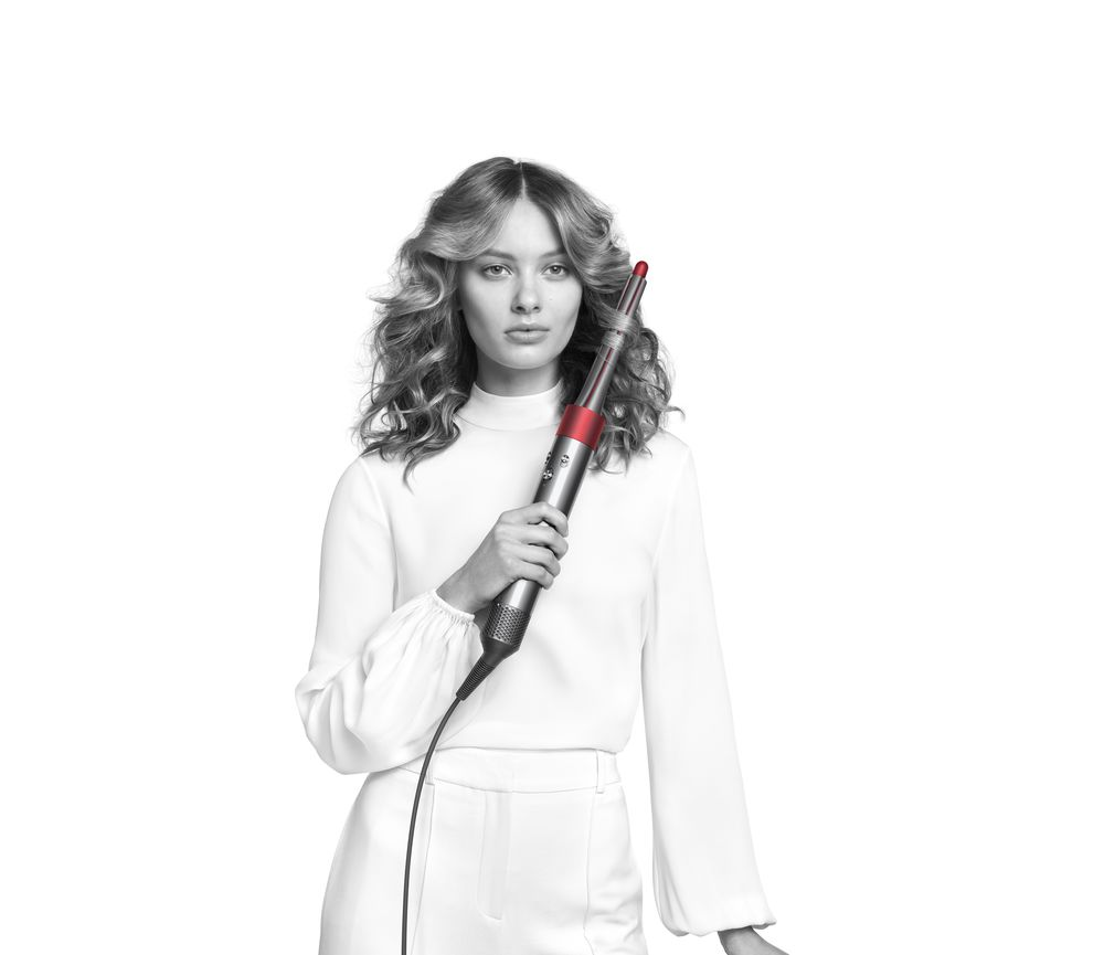 Vrouw houdt grijze en rode haarstylingtool vast, witte achtergrond.