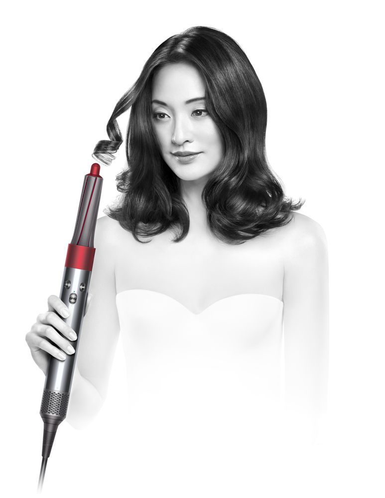 Vrouw met een Dyson haarstyler die een krul creëert. Ze draagt een witte top.