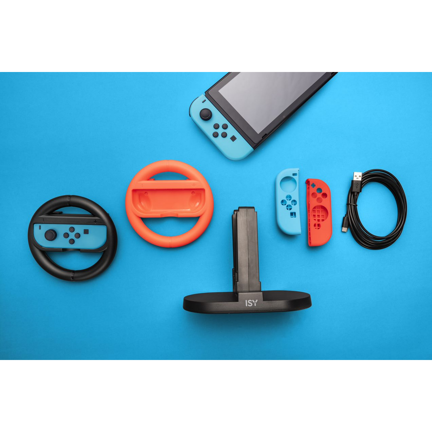 Accesorios de juego Switch: consola, dos mandos, volante, cargador y soporte, sobre fondo azul.
