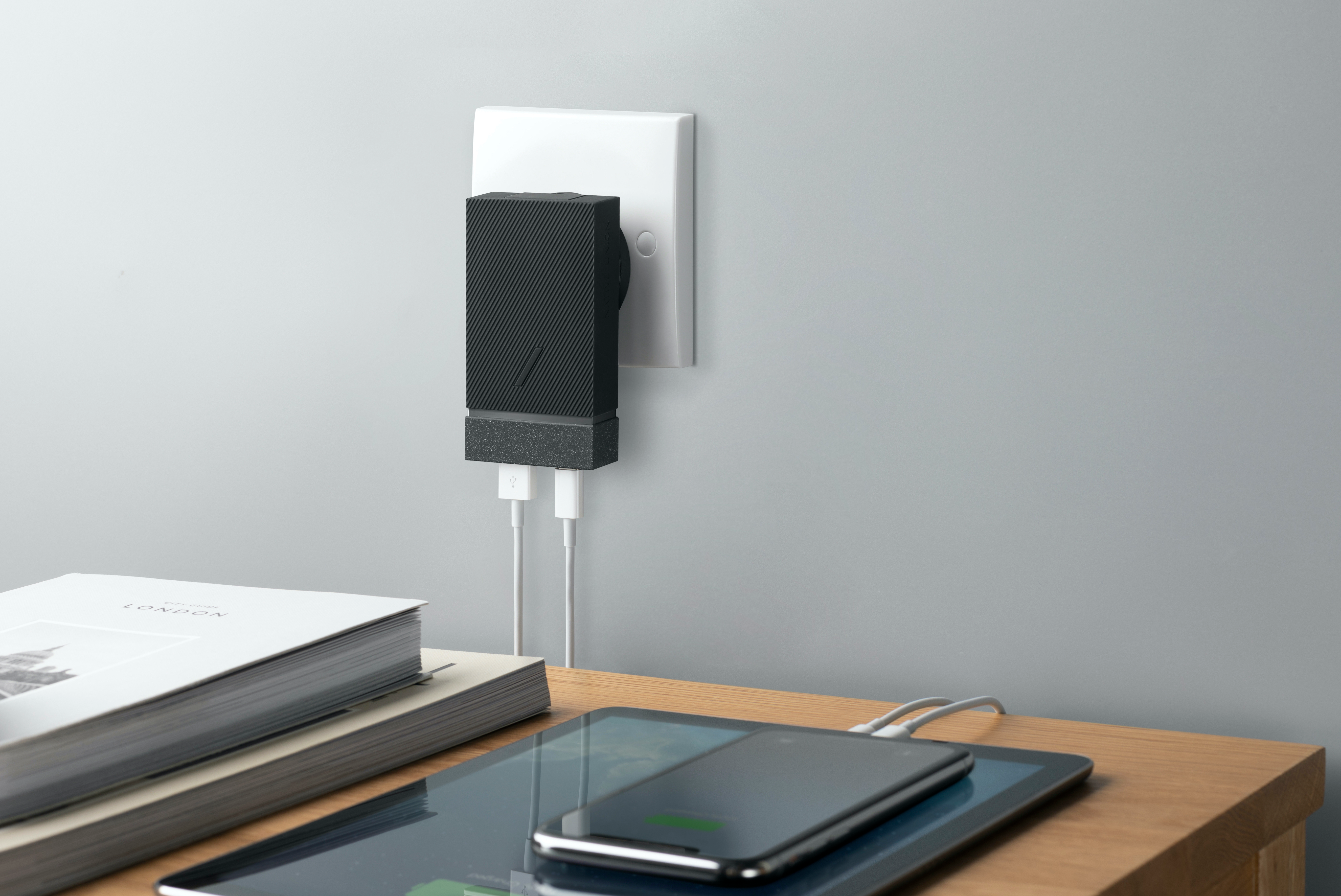 Caricabatterie nero collegato al muro, carica tablet e telefono.