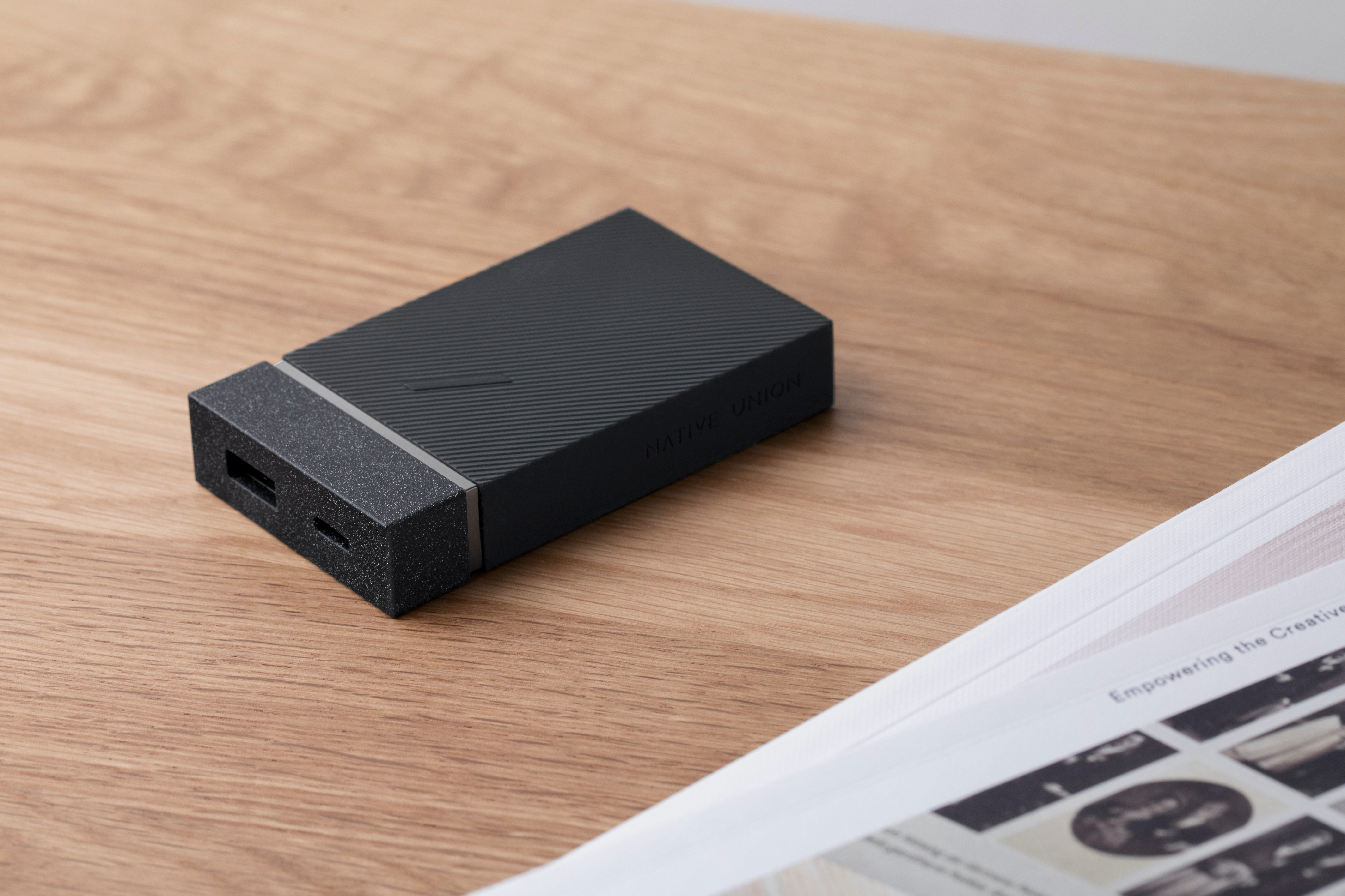 Power bank nero su un tavolo di legno, vicino a una rivista.