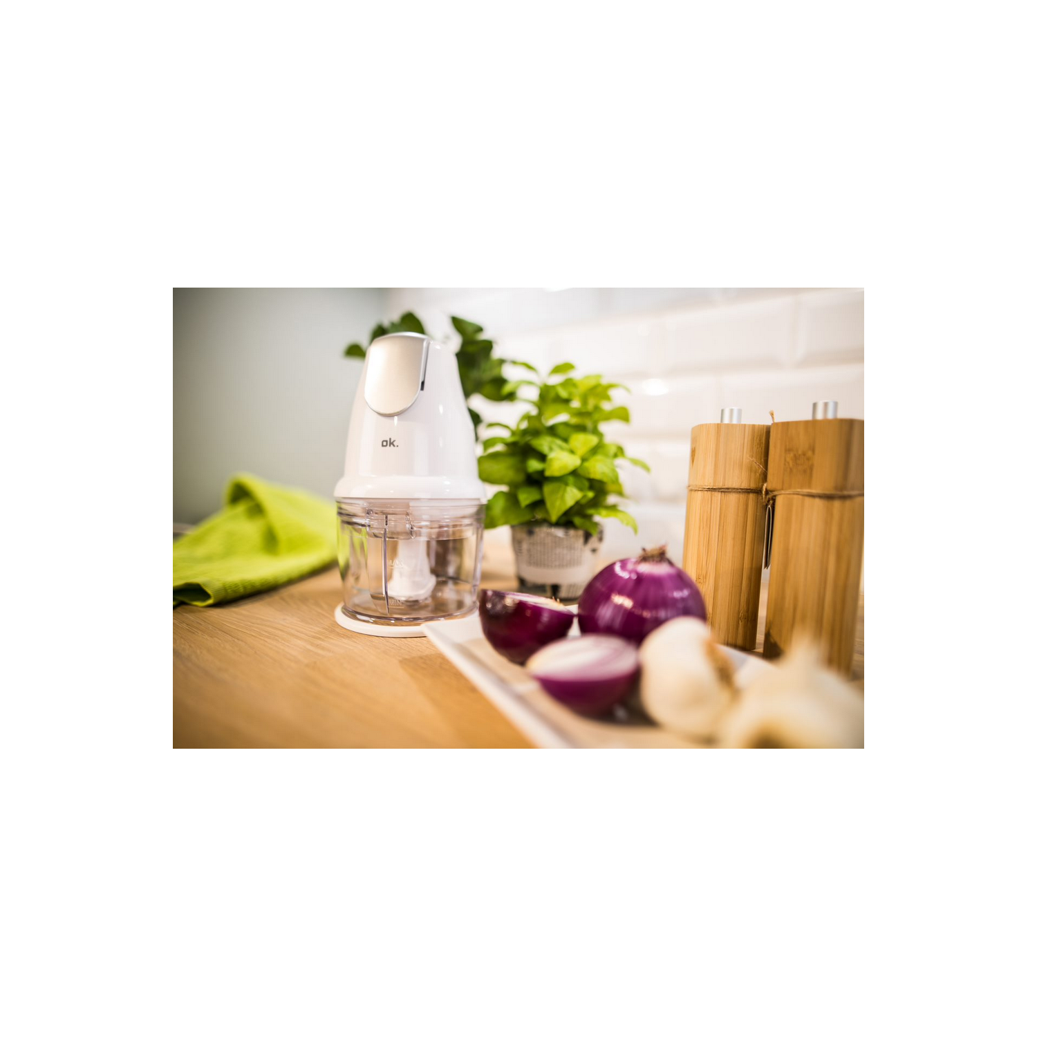 Picadora eléctrica blanca con ingredientes en una encimera de madera, plantas al fondo.