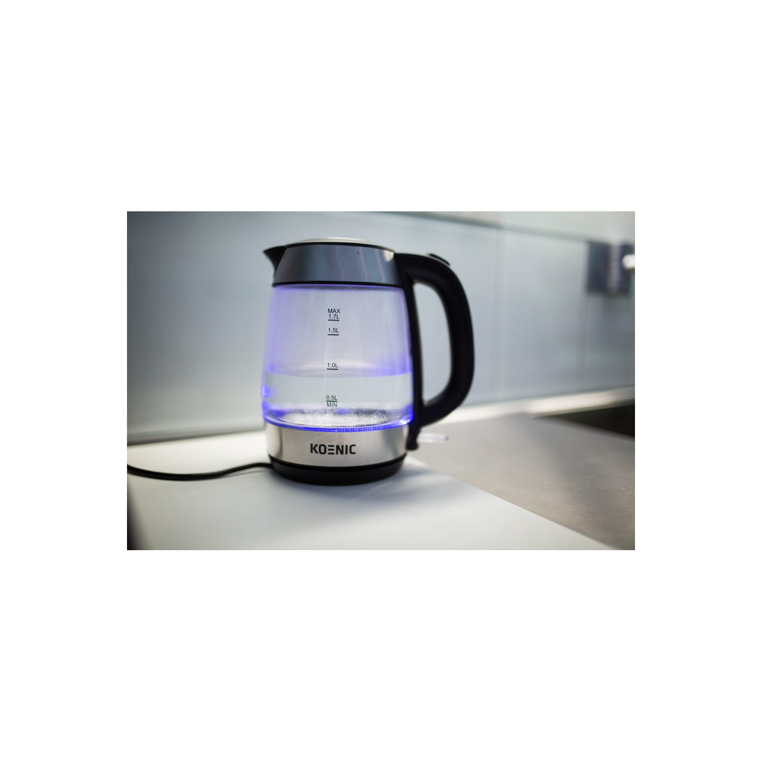 Una tetera eléctrica de vidrio transparente con agua adentro, iluminada por luces azules. La tetera está sobre una superficie blanca.