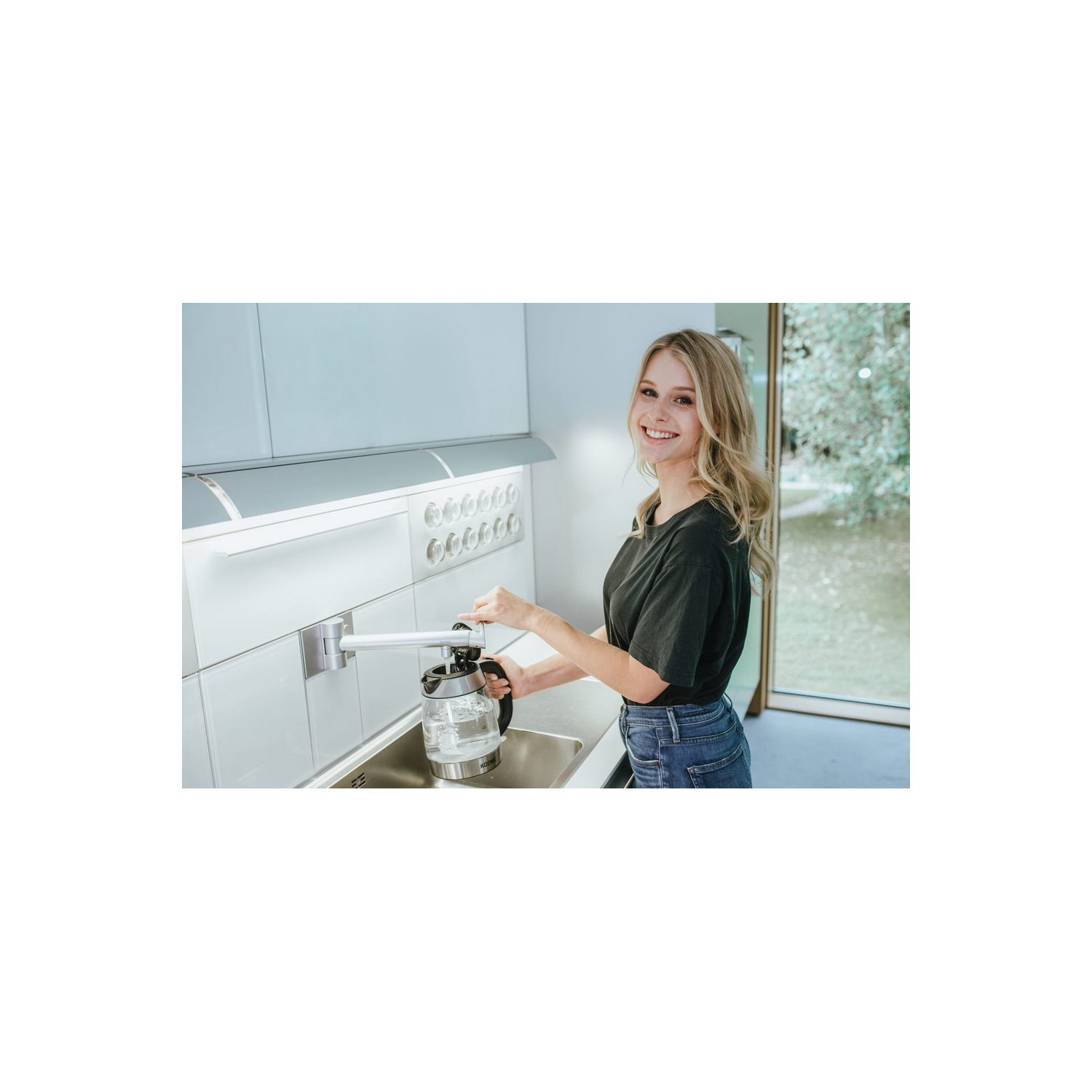 Una mujer llenando una jarra de agua cerca de un fregadero, con una lámpara de pared.