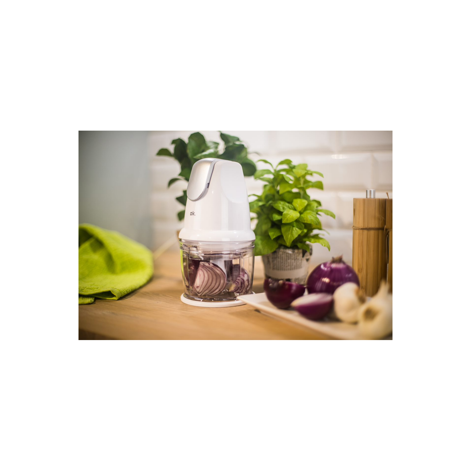Procesador de alimentos blanco con cebollas rojas y plantas verdes.