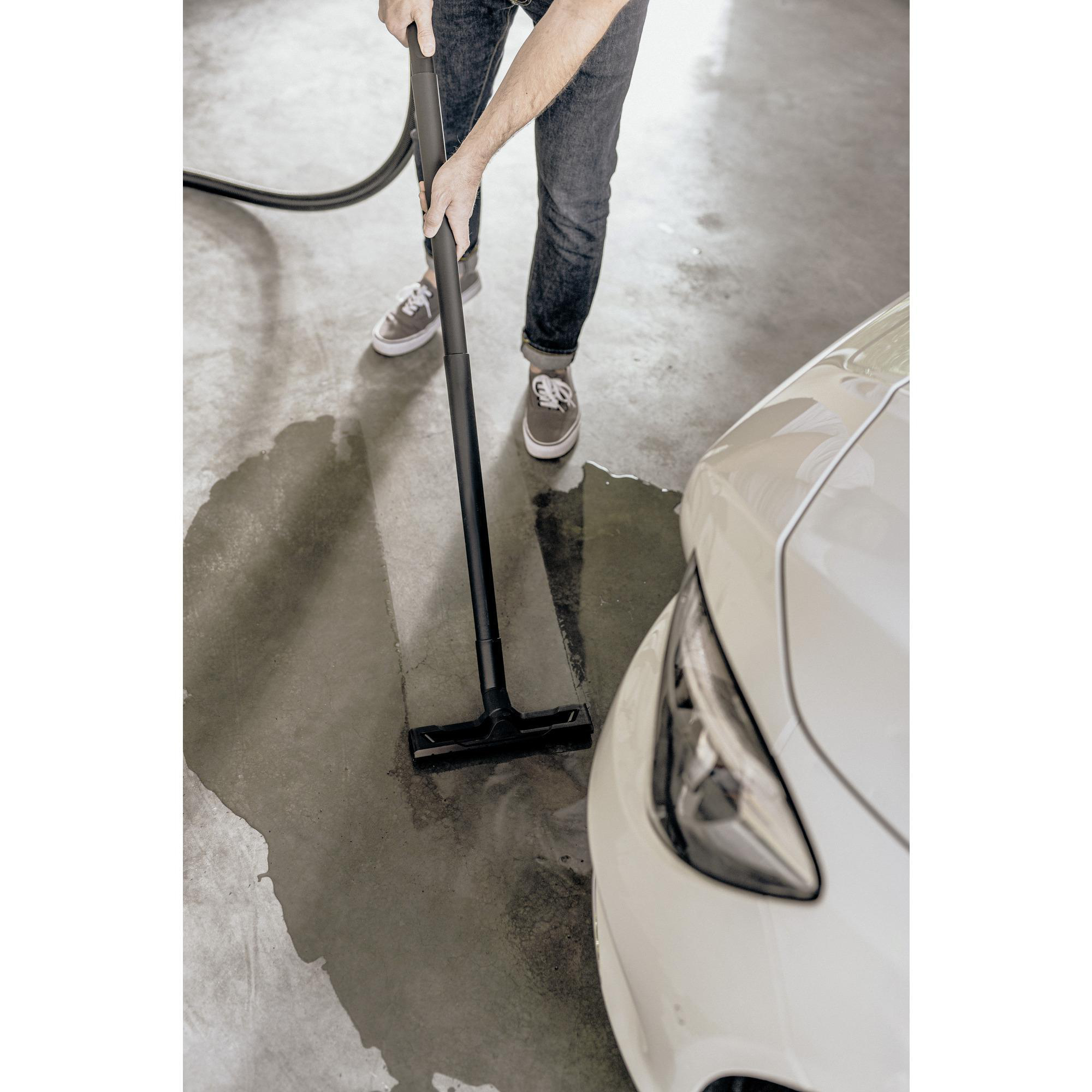 Person reinigt einen nassen Boden mit einem Staubsauger in der Nähe der Front eines weißen Autos.