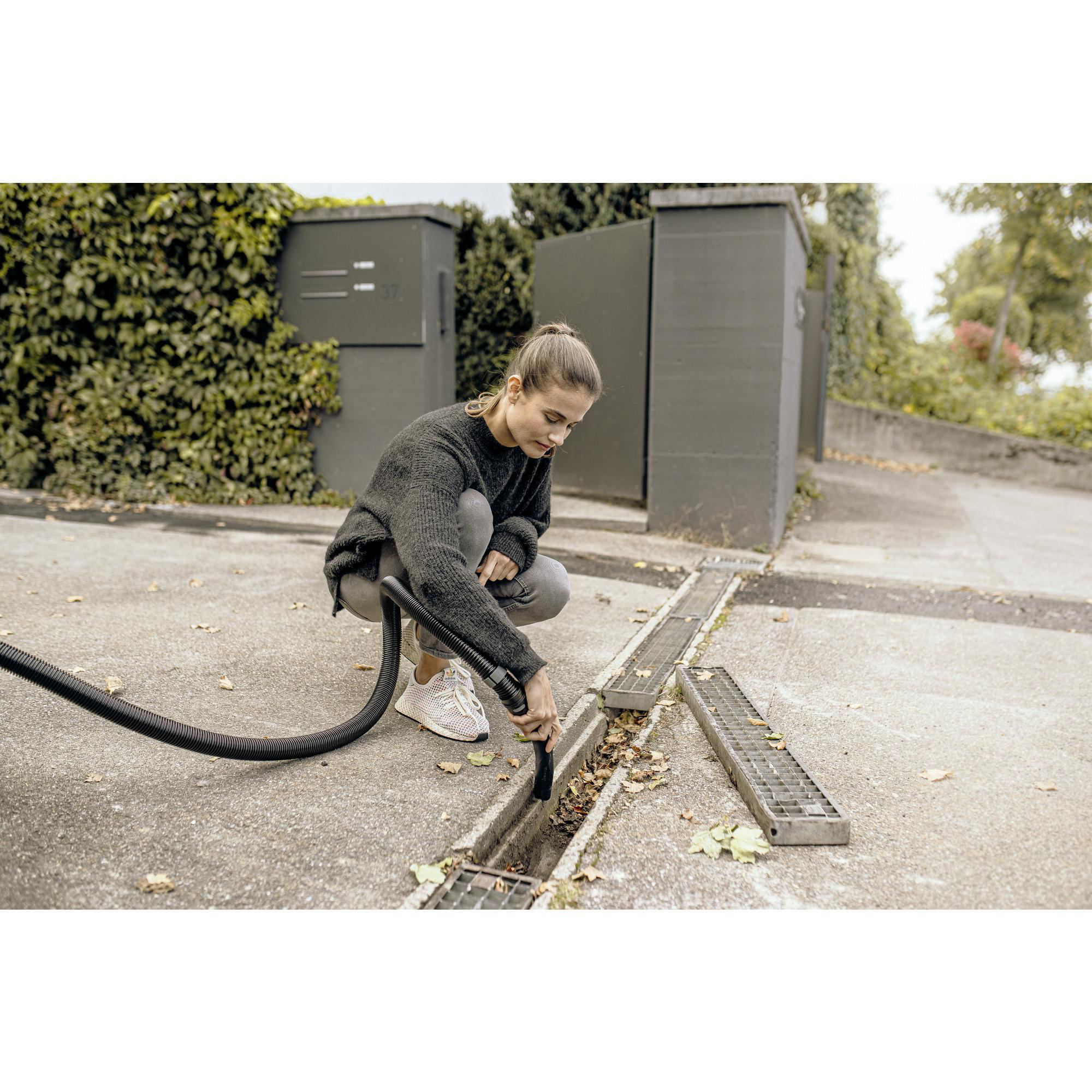 Frau reinigt Abfluss mit Staubsauger, Betonboden.