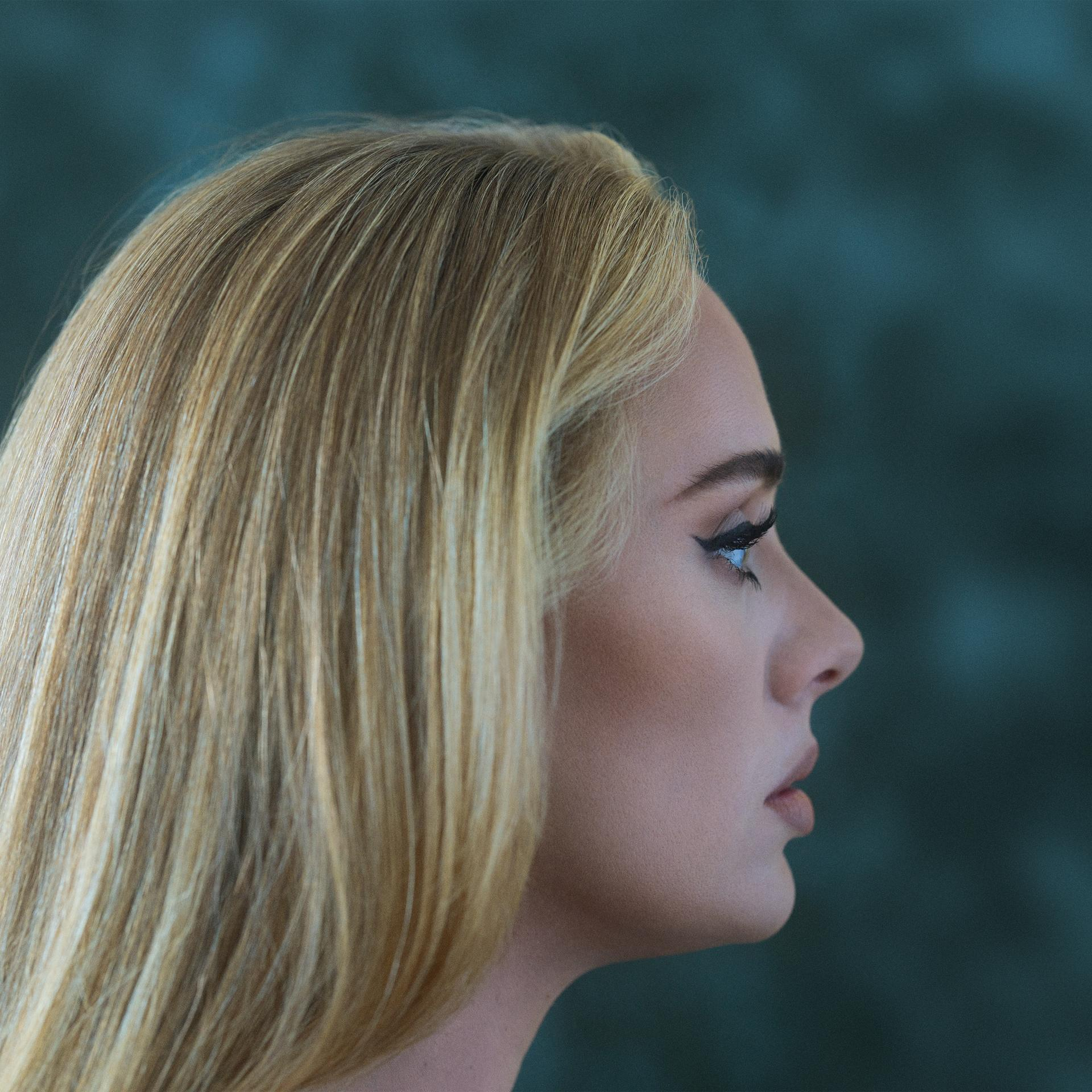 Zijprofiel van Adele, met blond haar en donkere eyeliner, tegen een blauwgroene achtergrond.