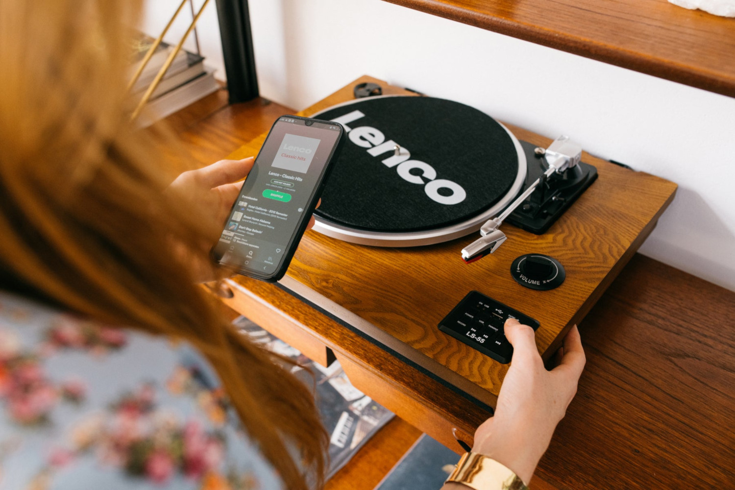 Personne utilisant un smartphone pour contrôler une platine. Logo Lenco sur la platine noire.