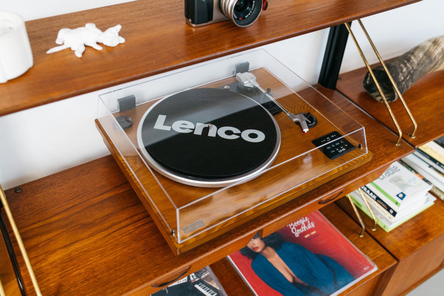 Étagère en bois avec une platine vinyle, des livres et un appareil photo. Pièce bien éclairée.
