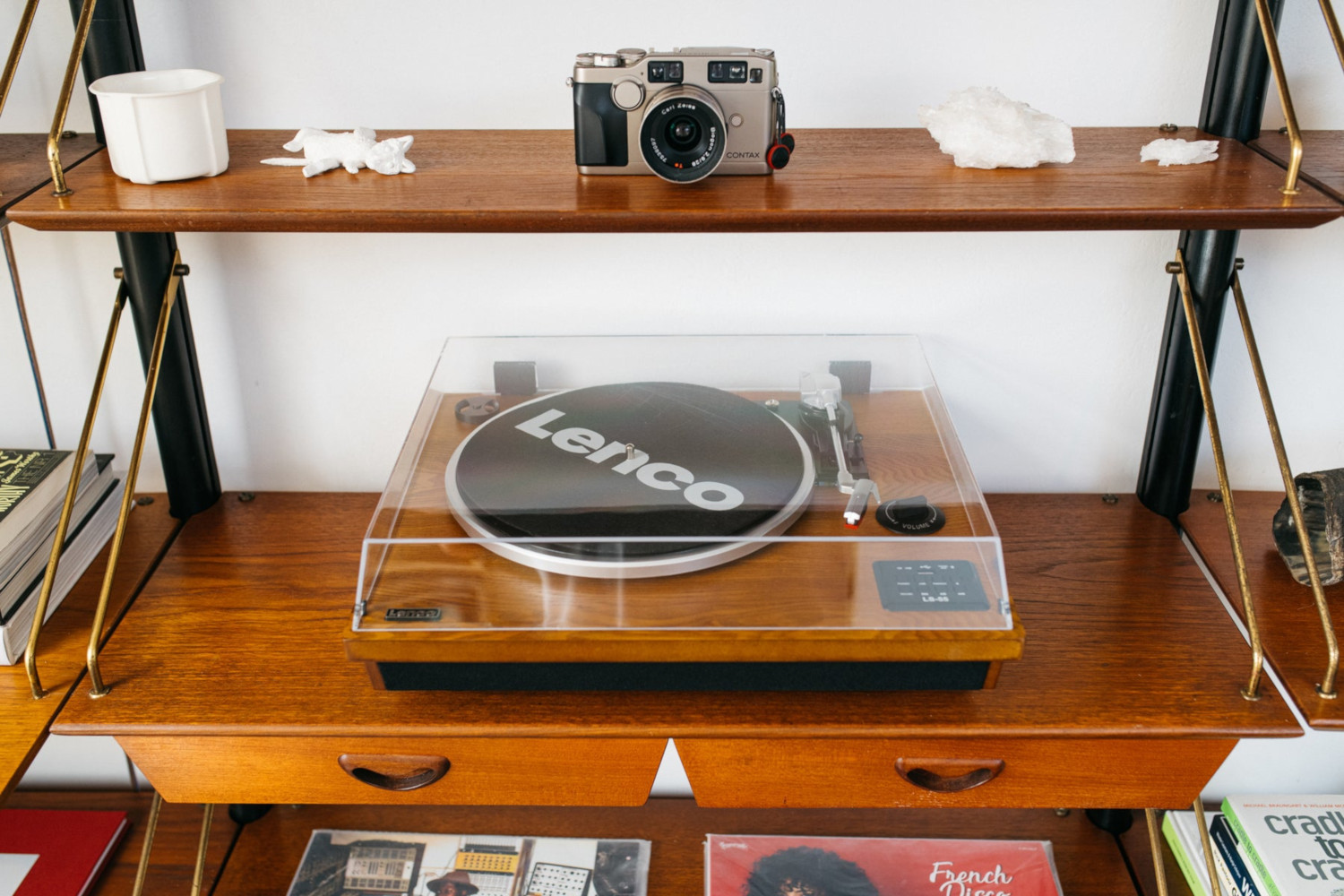 Une étagère en bois avec un appareil photo, un tourne-disque et d'autres objets. Le fond est blanc.