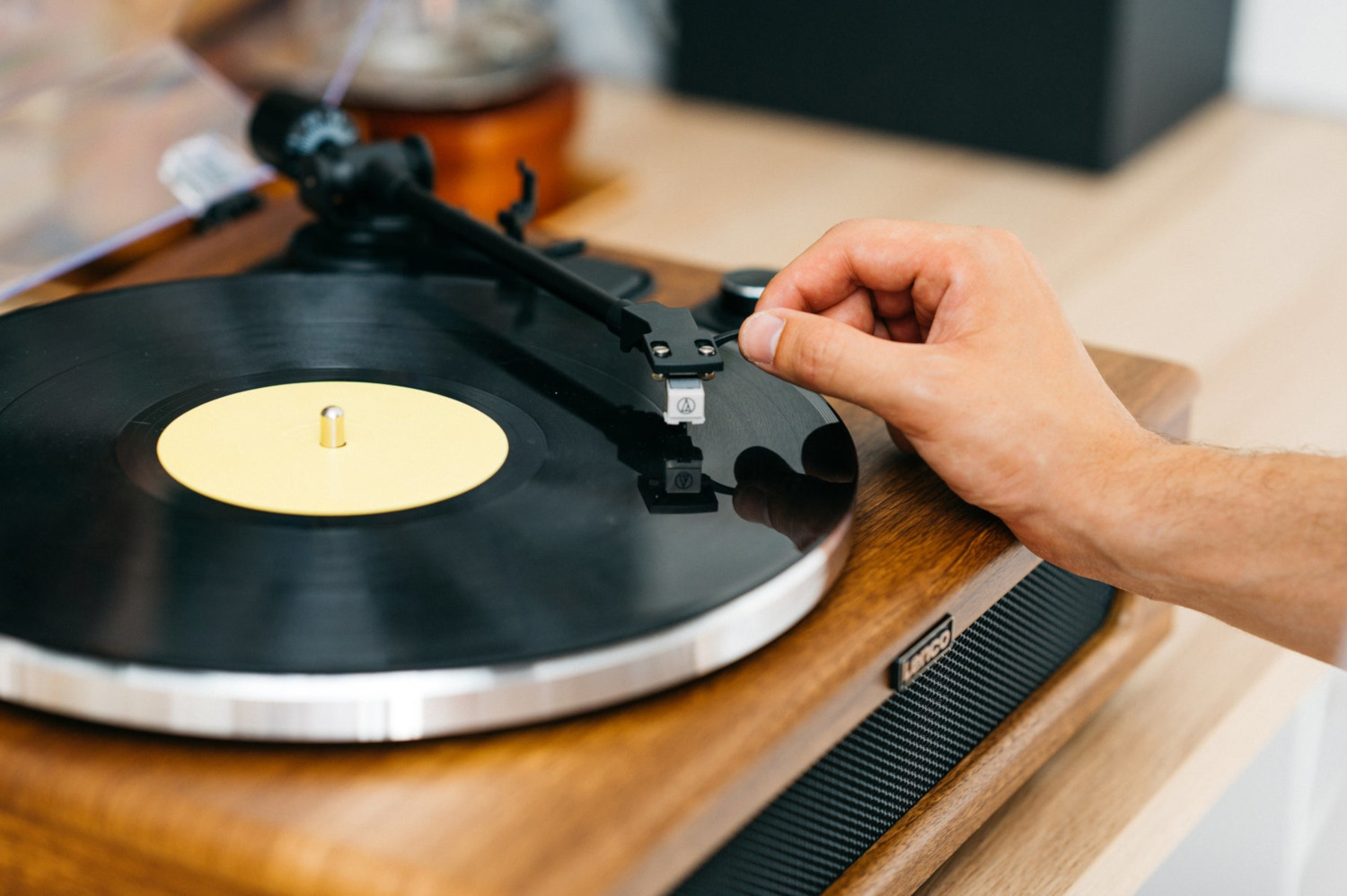 Een hand plaatst de naald op een zwarte vinylplaat op een houten platenspeler.