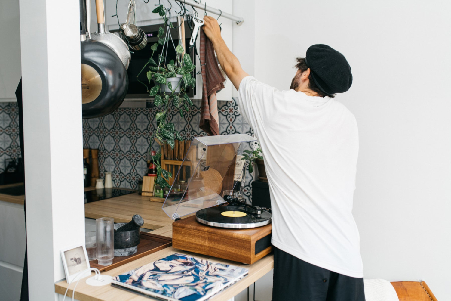 Een man in een keuken die een doek ophangt. Keuken omvat planten, platenspeler en kookgerei.