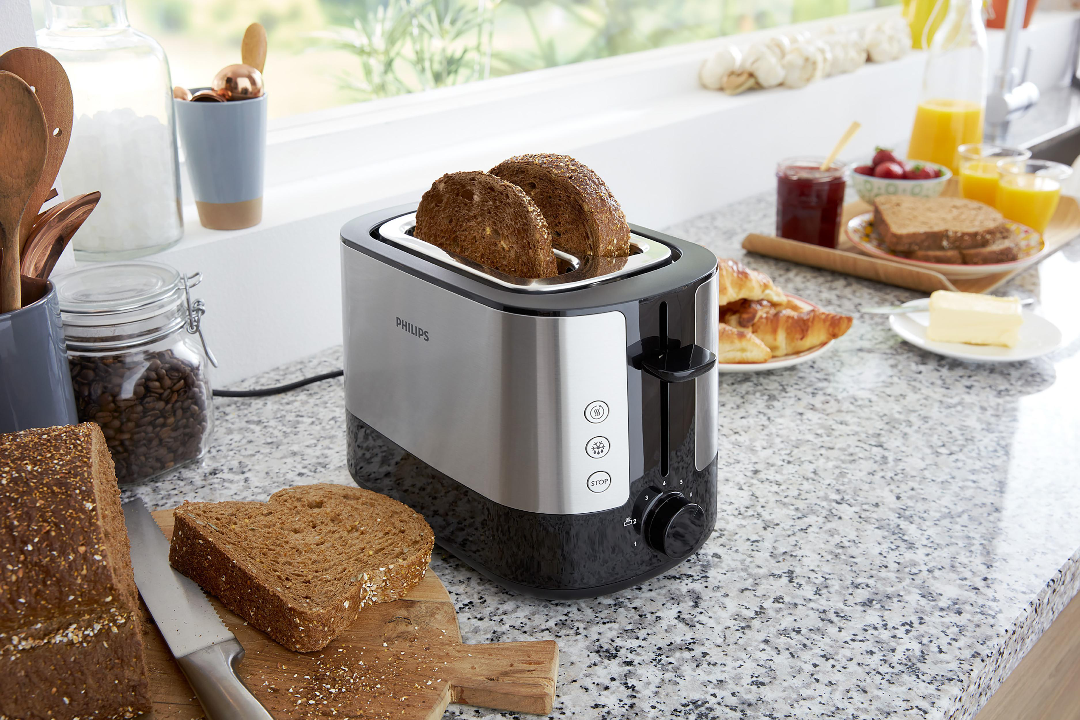 Toaster mit zwei Brotscheiben. Andere Lebensmittel sind im Hintergrund.